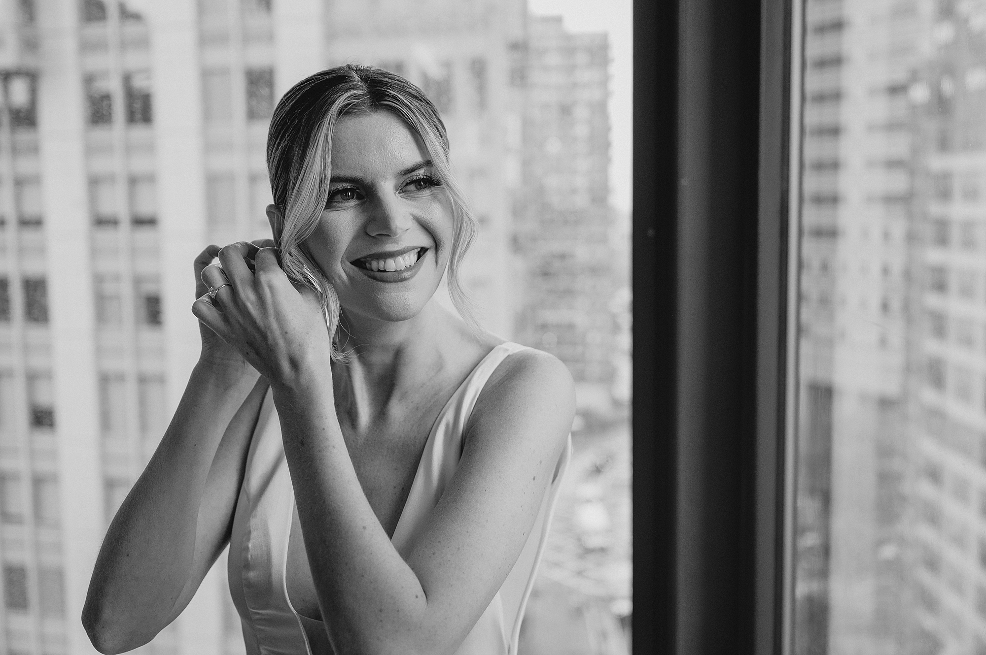 bride puts on earrings in front of window of Jersey City hotel