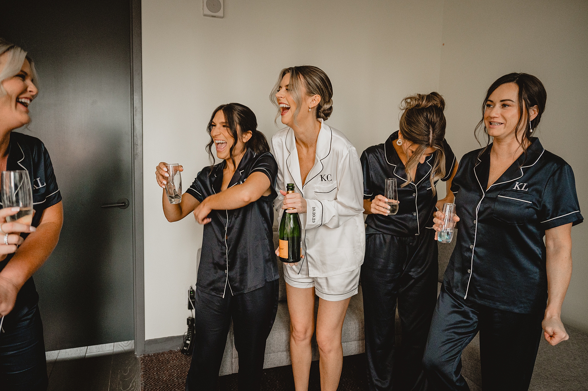 bride and bridesmaids laugh as champagne pops during wedding day in Jersey City