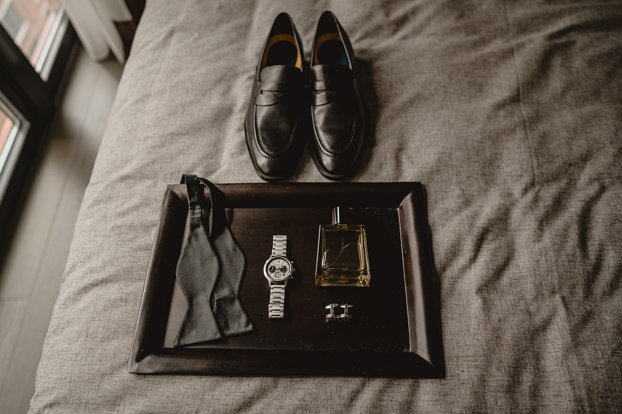groom's black shoes sit next to tray with tie, watch, and cologne