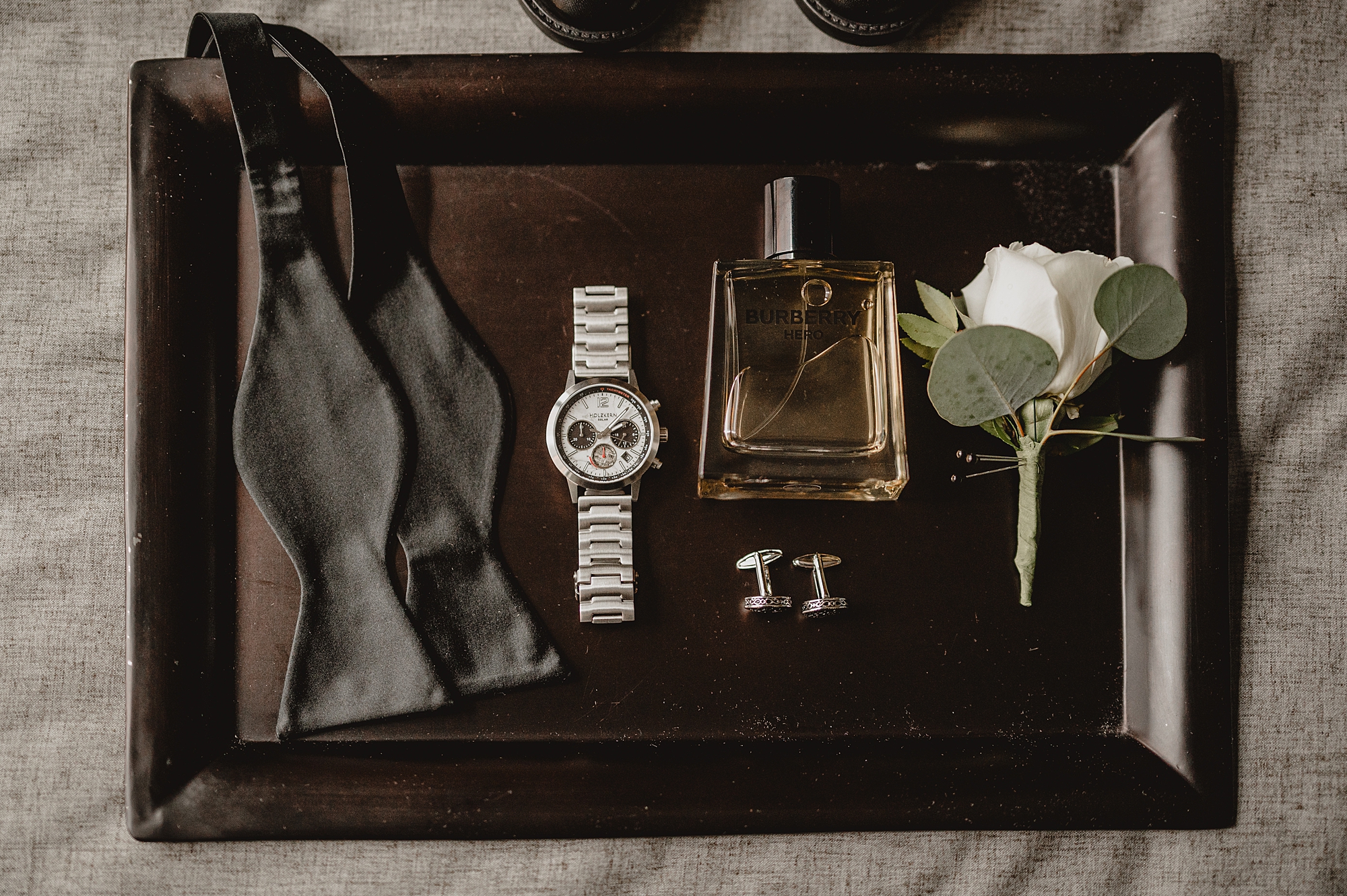 groom's bowtie, watch, cologne, and white rose boutineere on tray