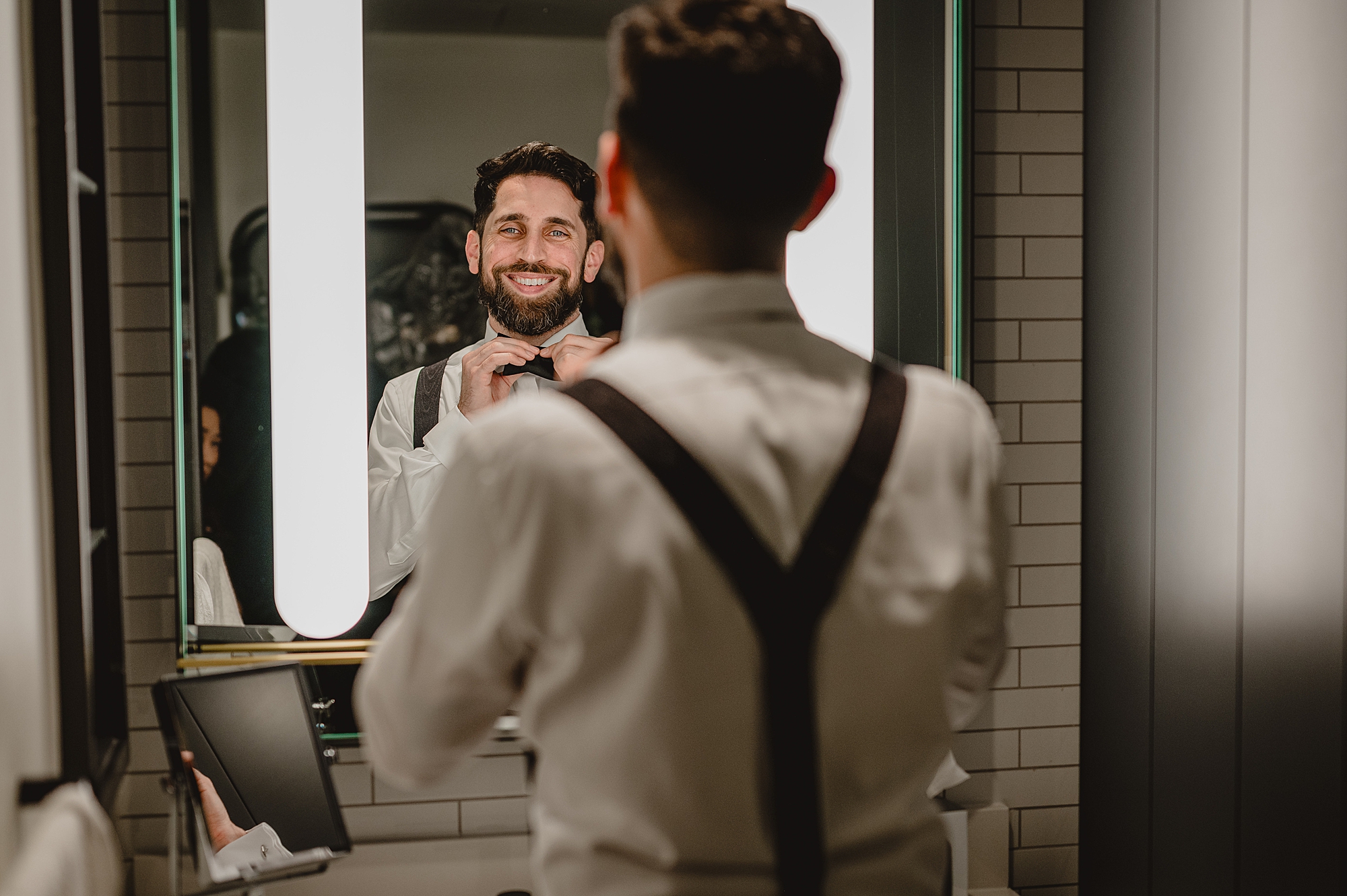 groom smiles adjusting bowtie before NJ wedding day