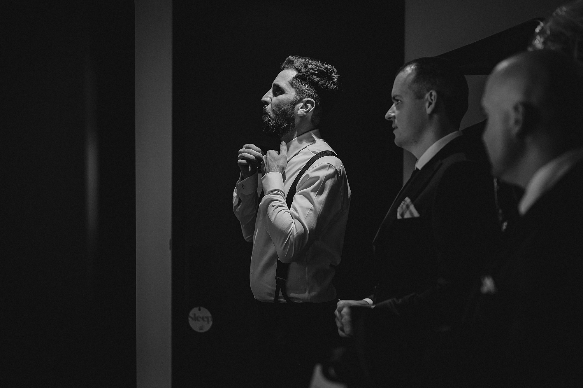 groomsmen look at groom adjusting tie in Jersey City hotel