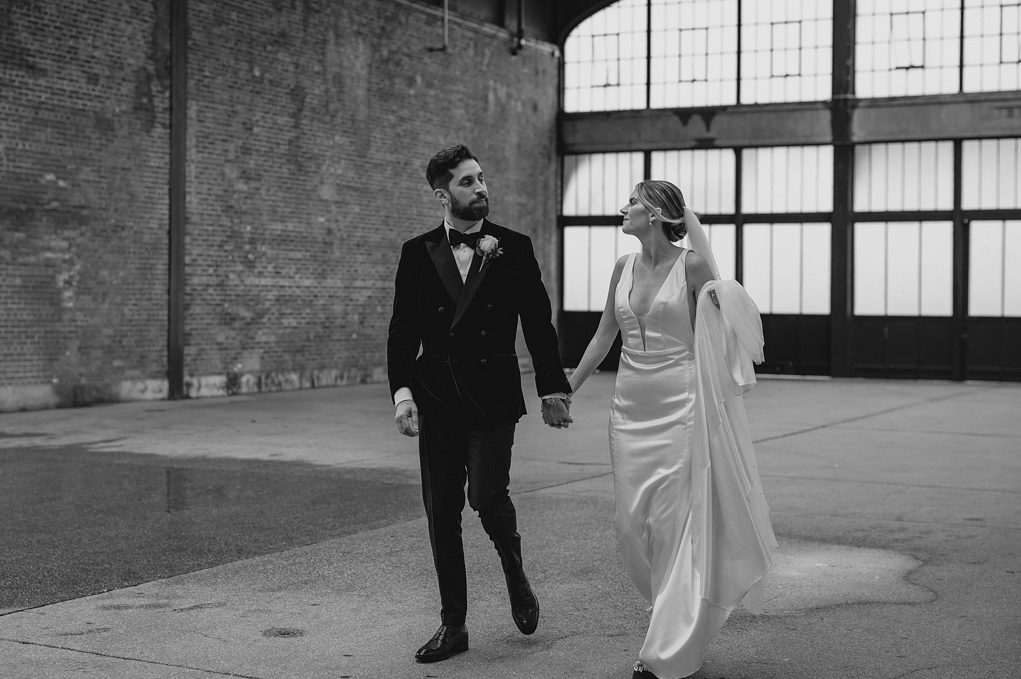 bride holds edge of wedding dress skirt while walking with groom