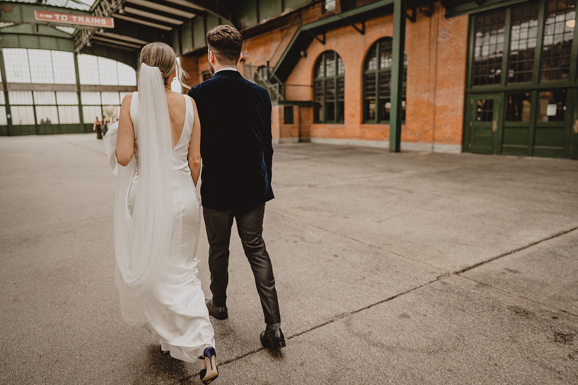 newlyweds hold hands walking towards Hudson River outside Maritime Parc