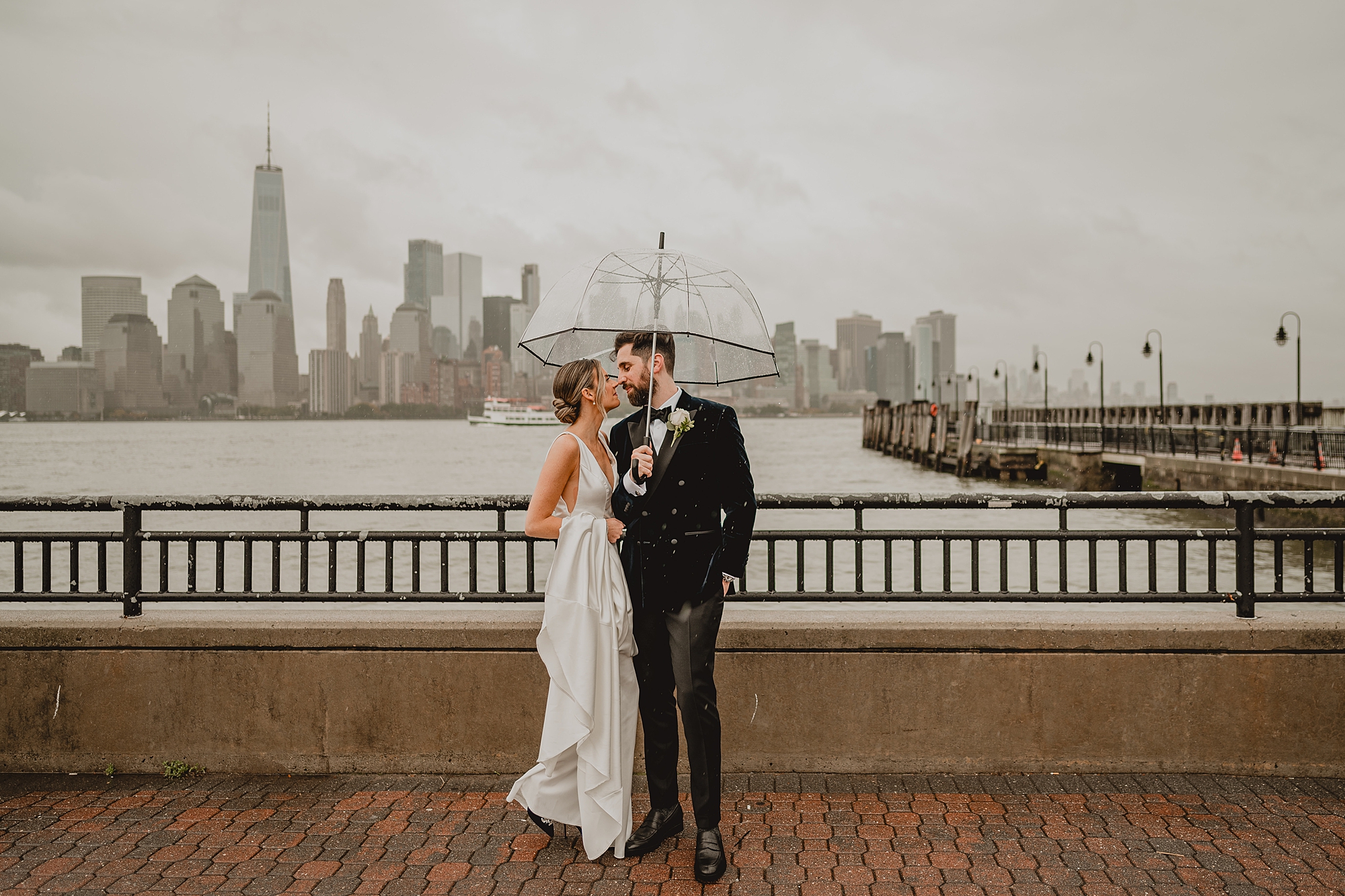 bride and groom hug under umbrella in front of Hudson River