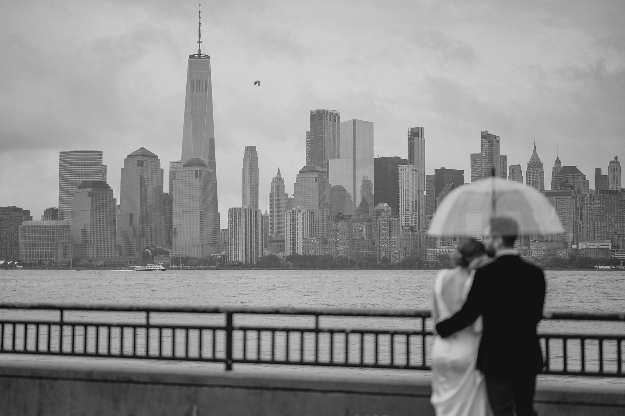 newlyweds hug under clear umbrella during rainy wedding at Maritime Parc