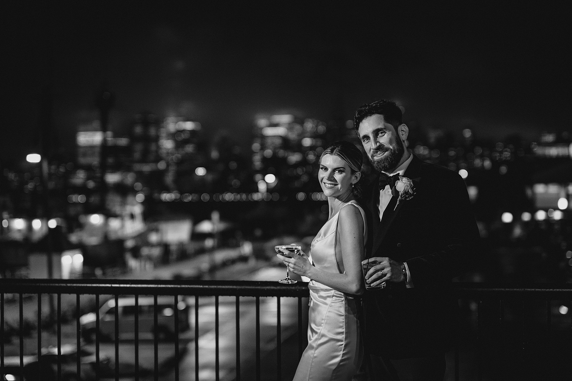 newlyweds hold drinks on balcony overlooking NYC skyline