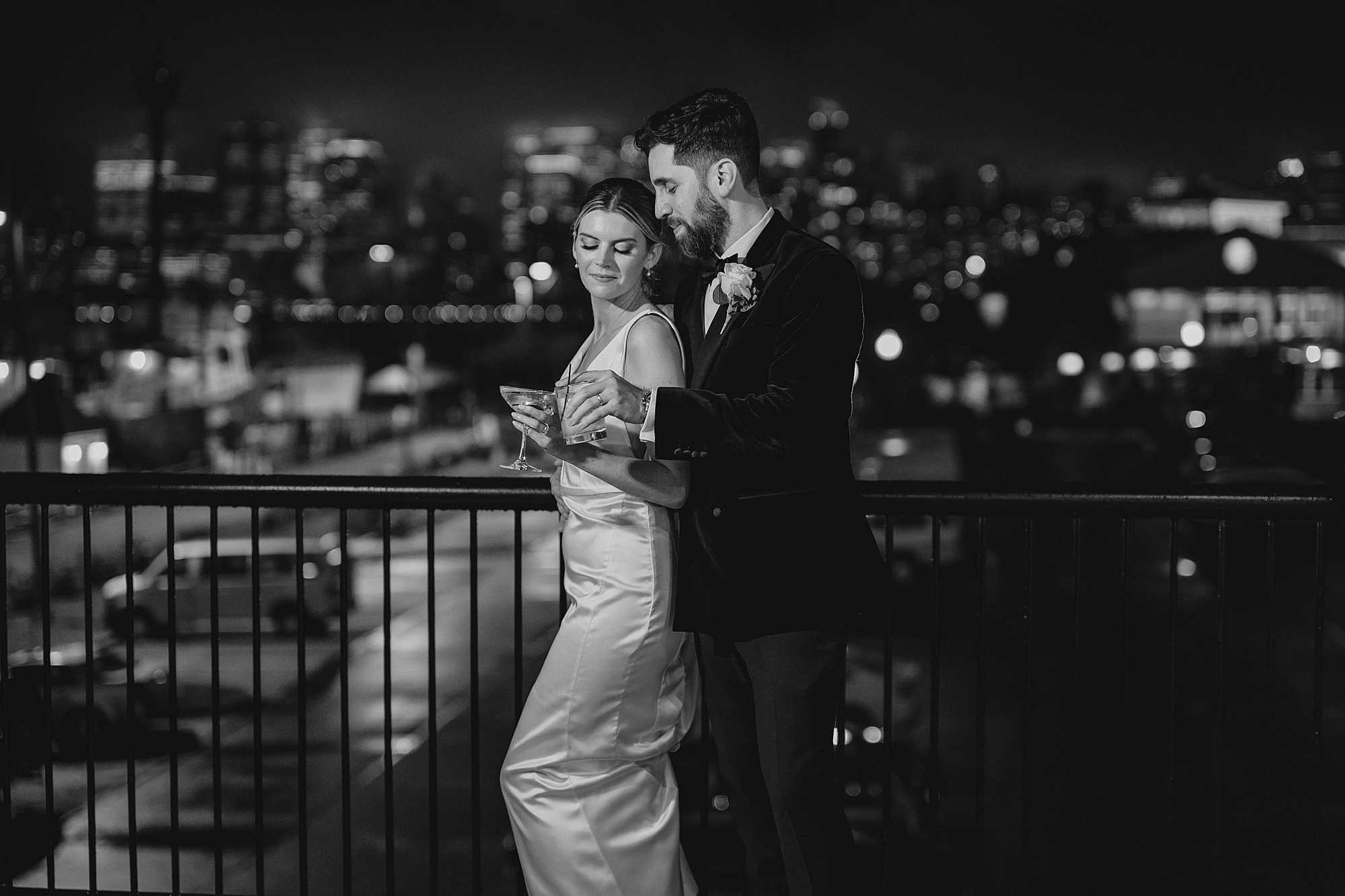 newlyweds hold drinks on balcony overlooking NYC skyline