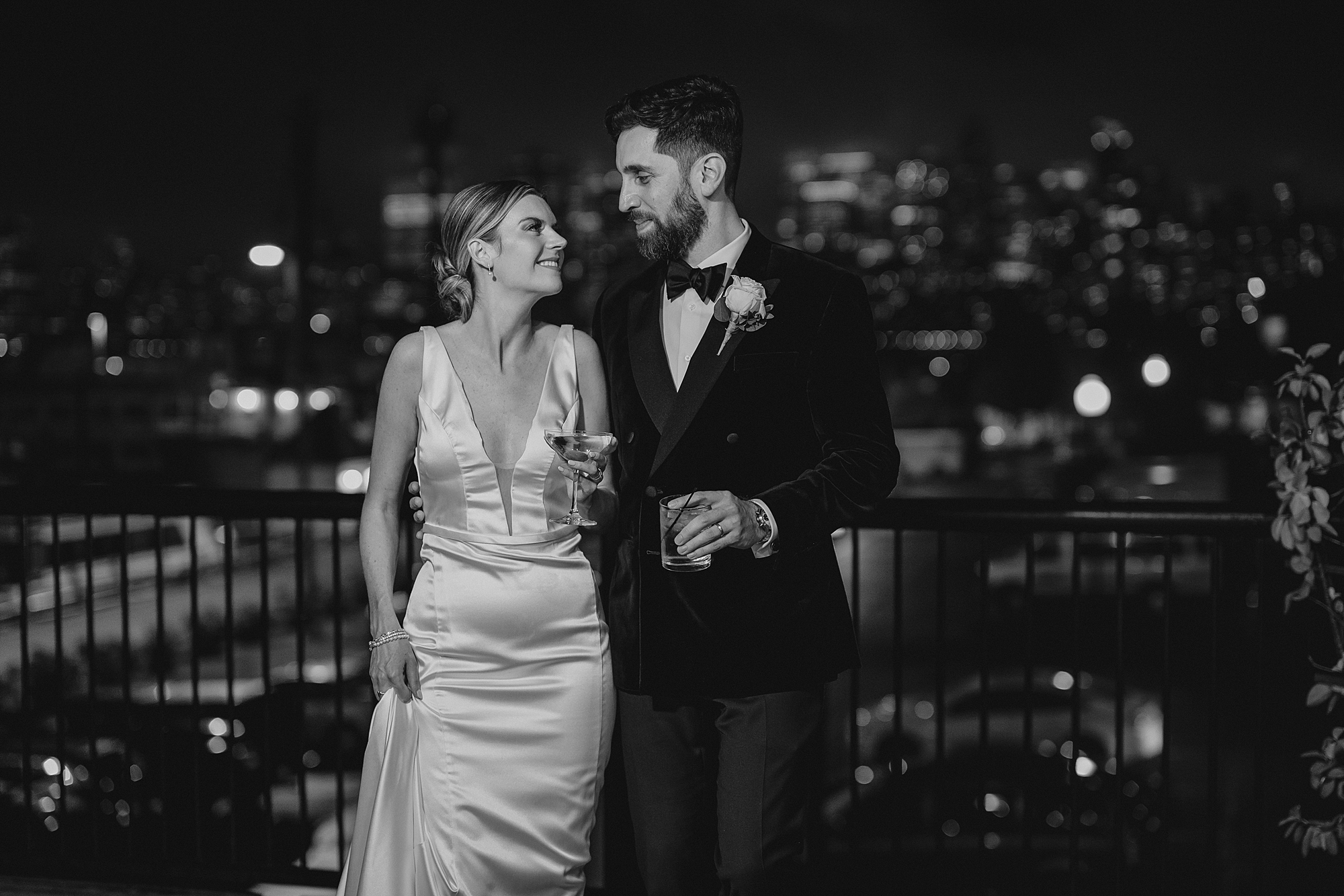 newlyweds hold drinks on balcony overlooking NYC skyline