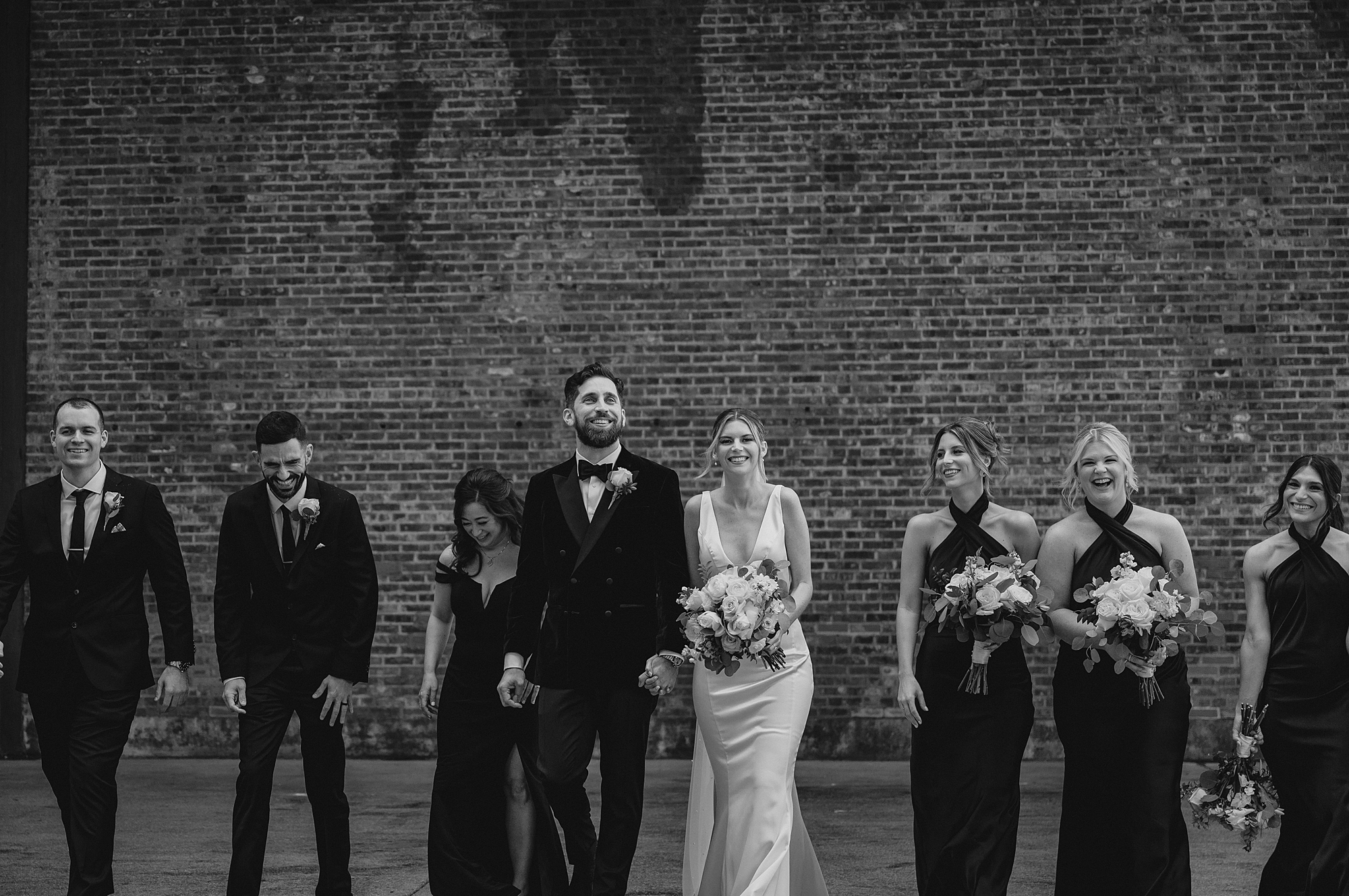 newlyweds stand with wedding party beside brick wall at Maritime Parc