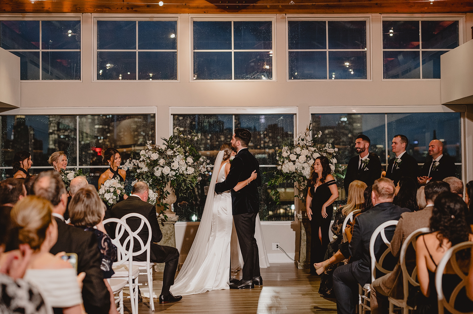 newlyweds kiss at Maritime Parc during ceremony in front of white wall of windows