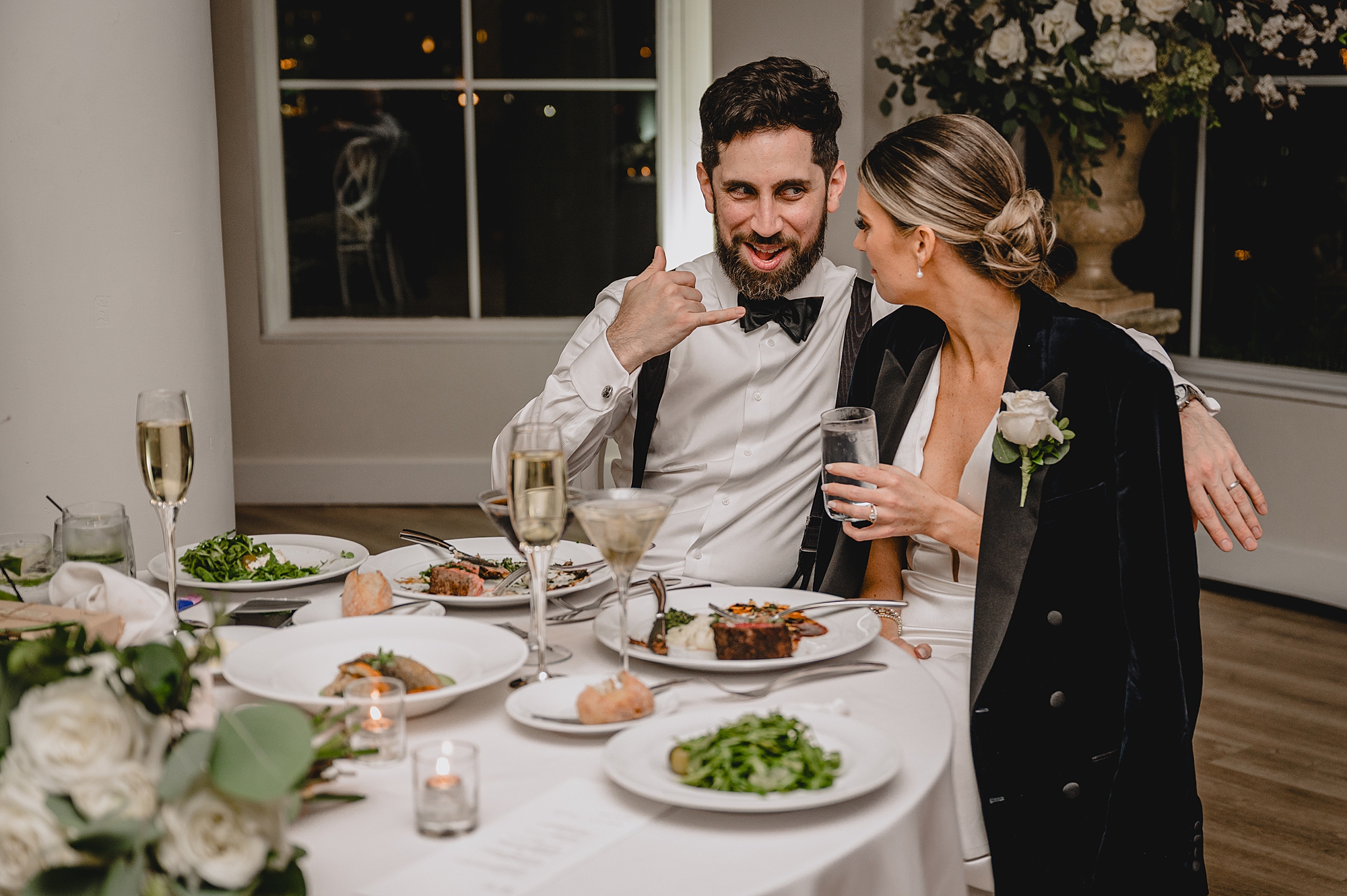 bride and groom eat dinner together with bride wearing groom's jacket