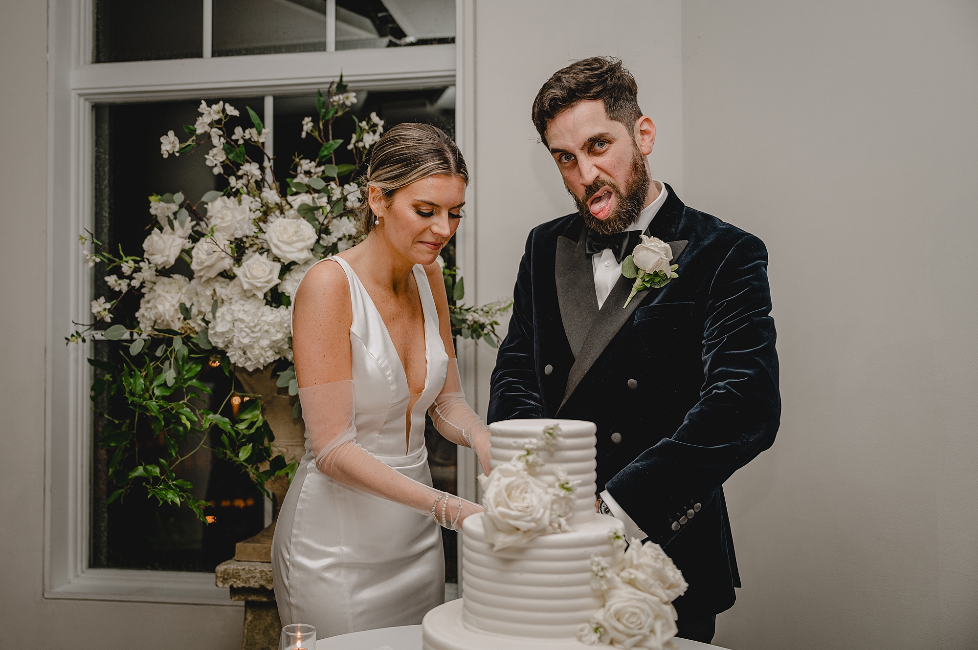 bride and groom cut tiered wedding cake and make silly faces
