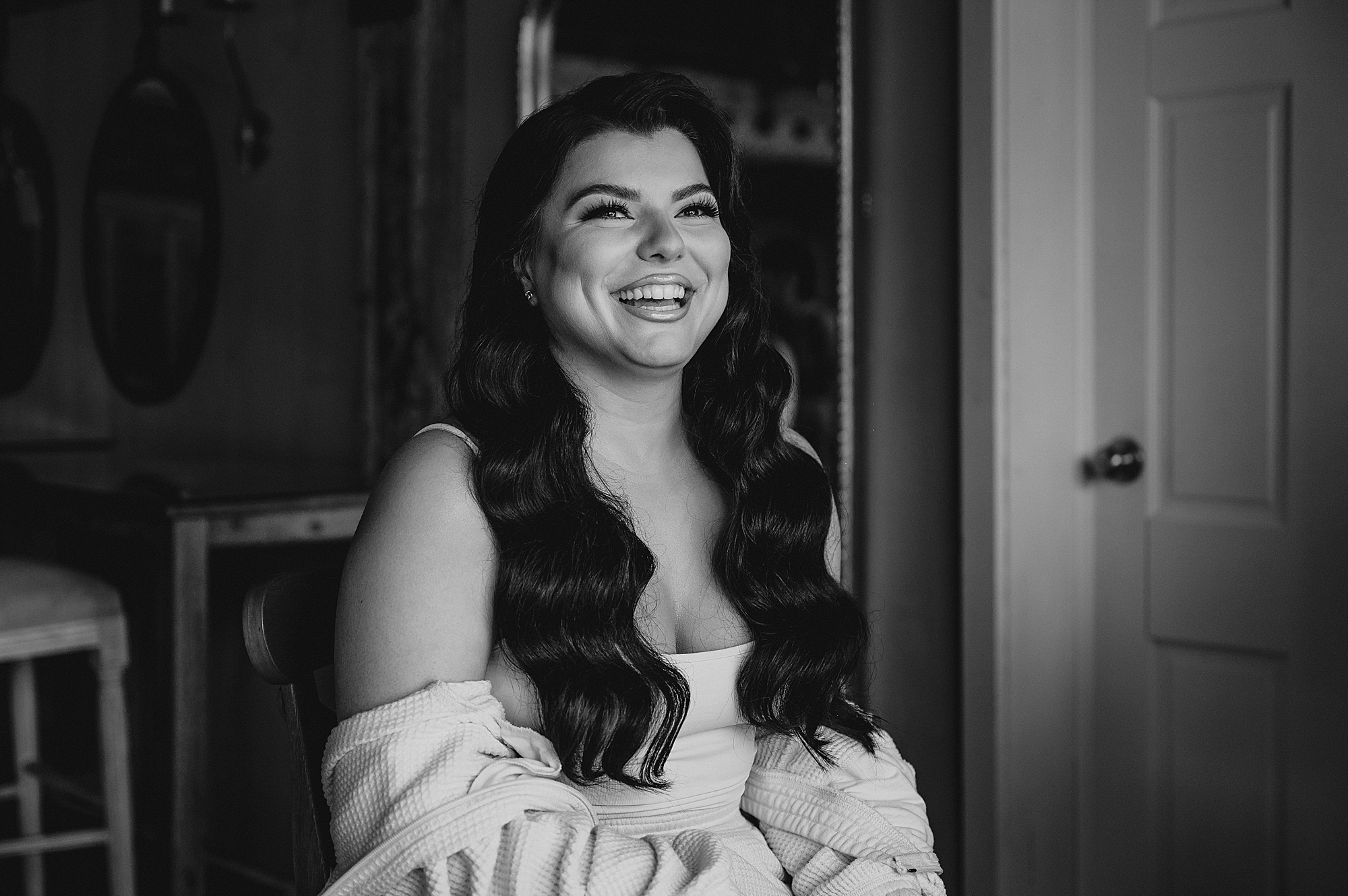 brunette bride smiles in off-the-shoulder shirt on wedding morning