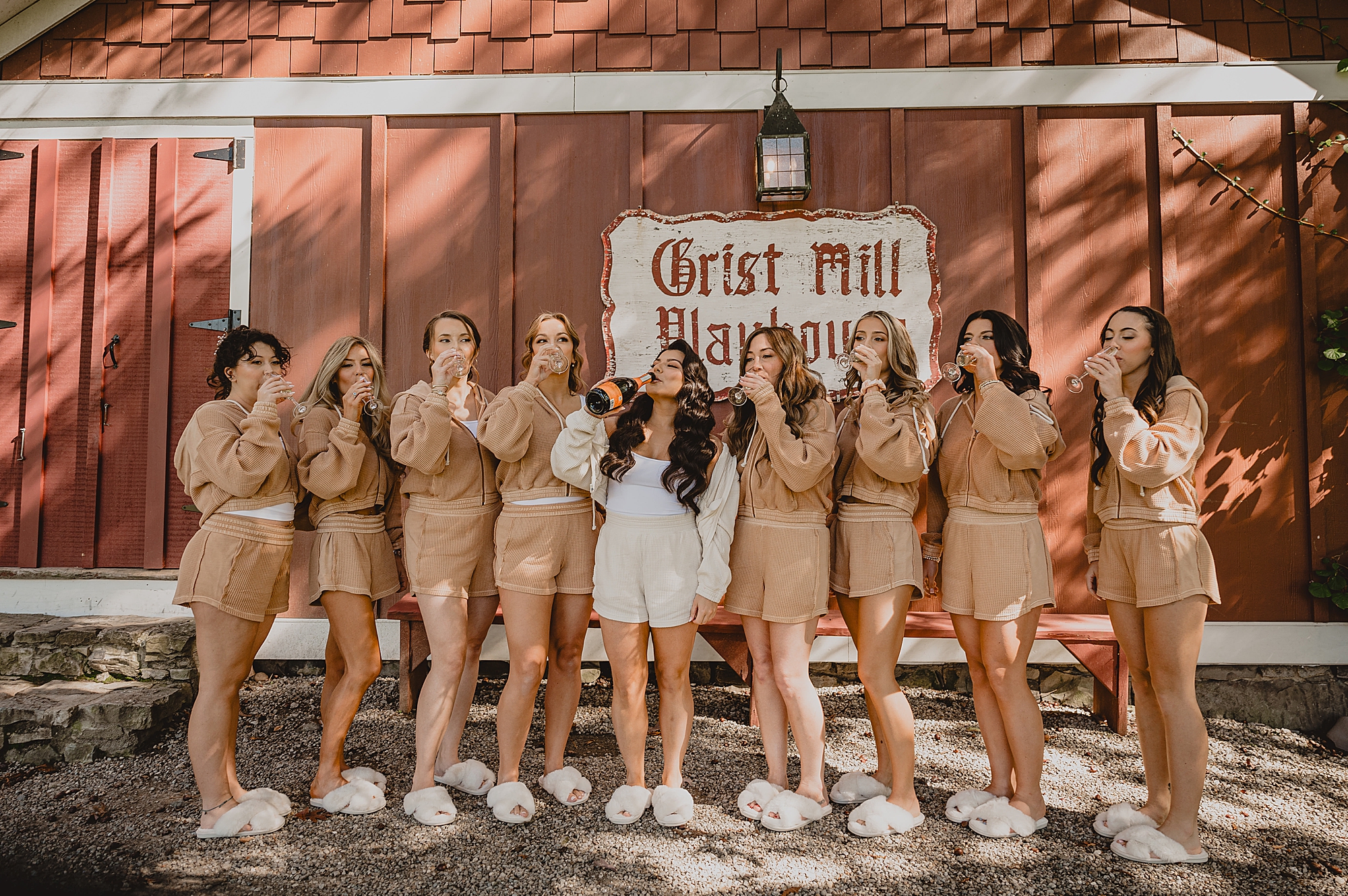 bride and bridesmaids drink champagne together outside the Grist Mill at Crossed Keys Estate