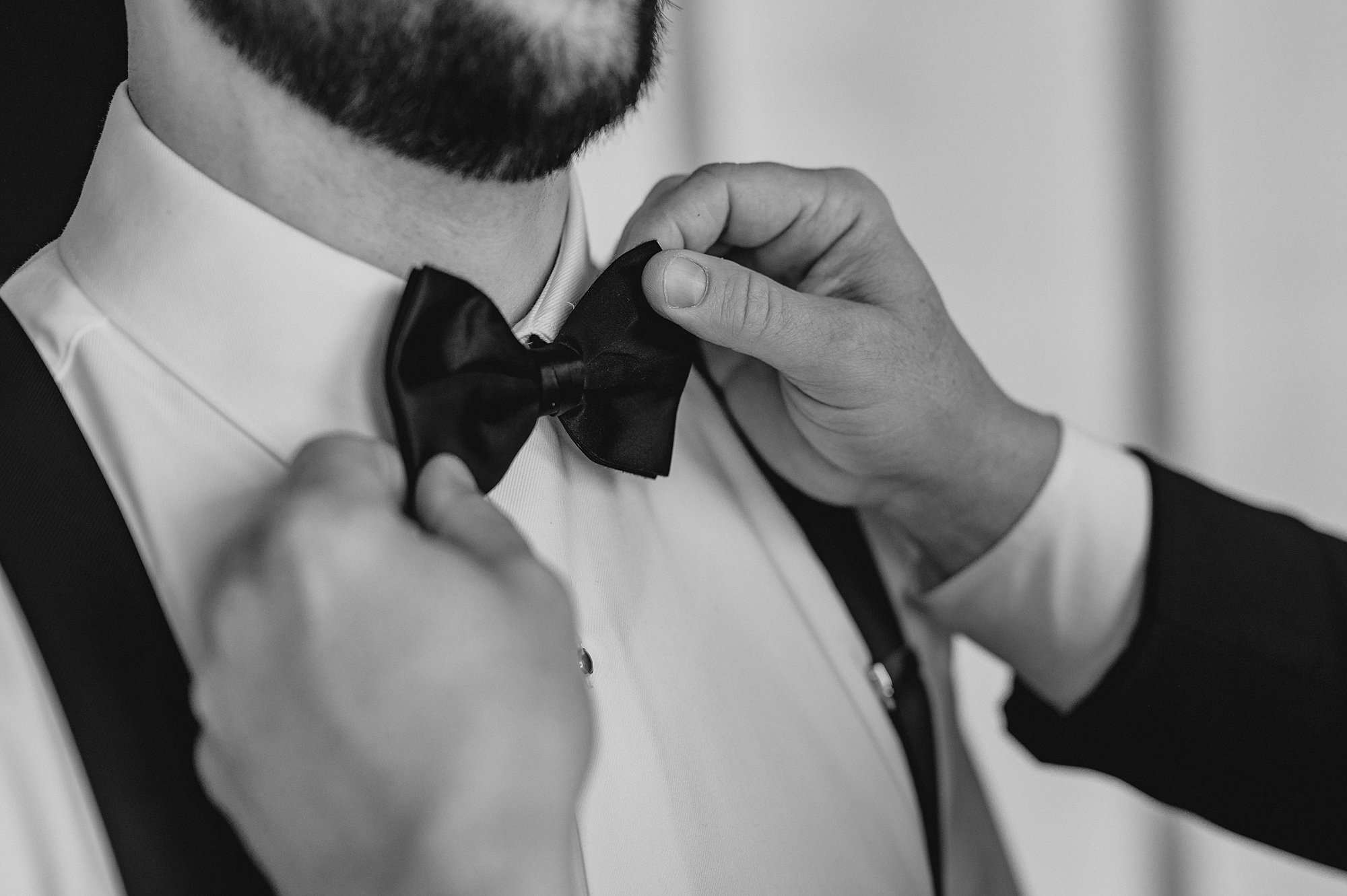 groomsman adjusts bowtie for groom on wedding day
