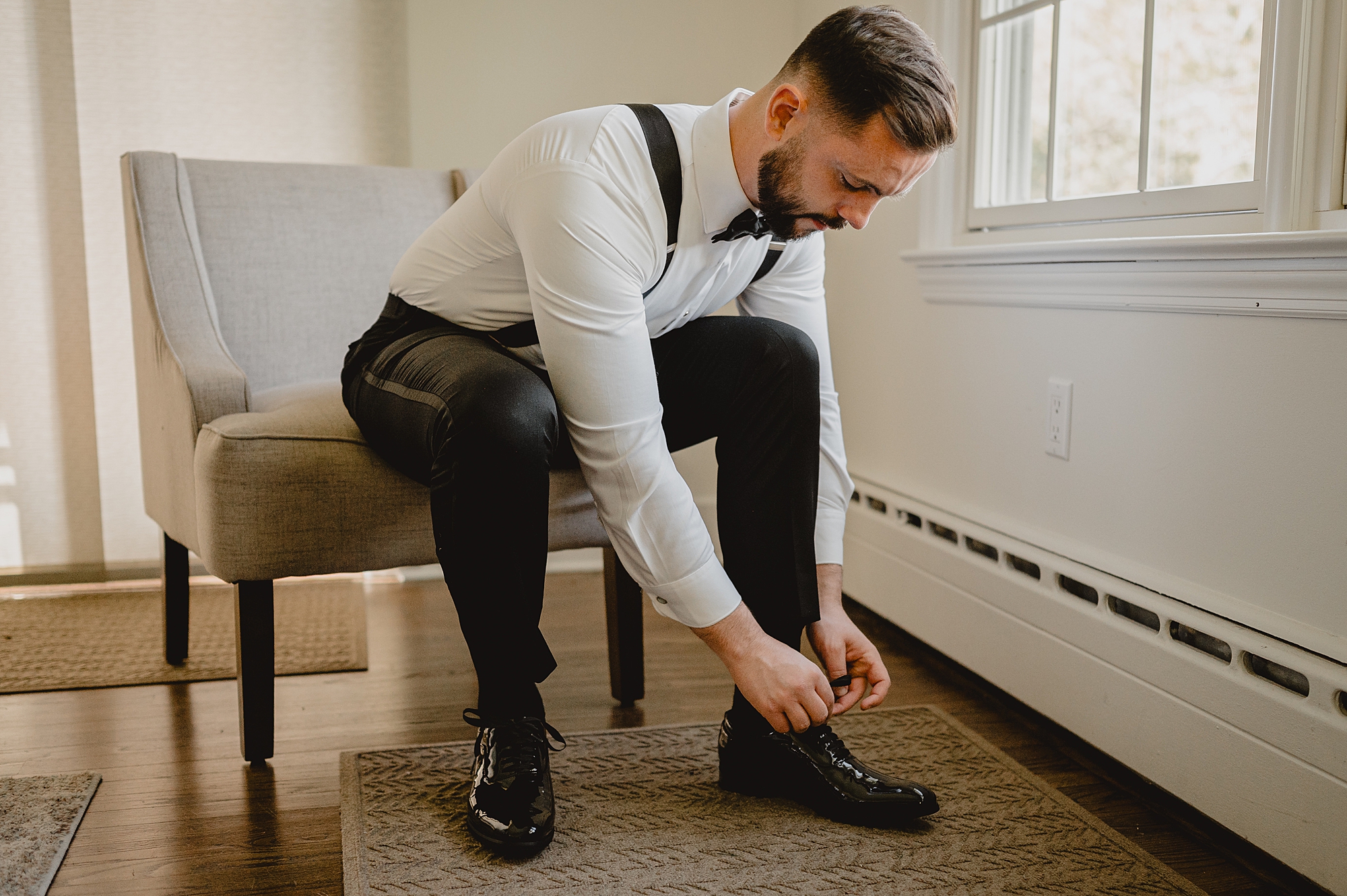 groom sits, tying black shoes on morning of wedding