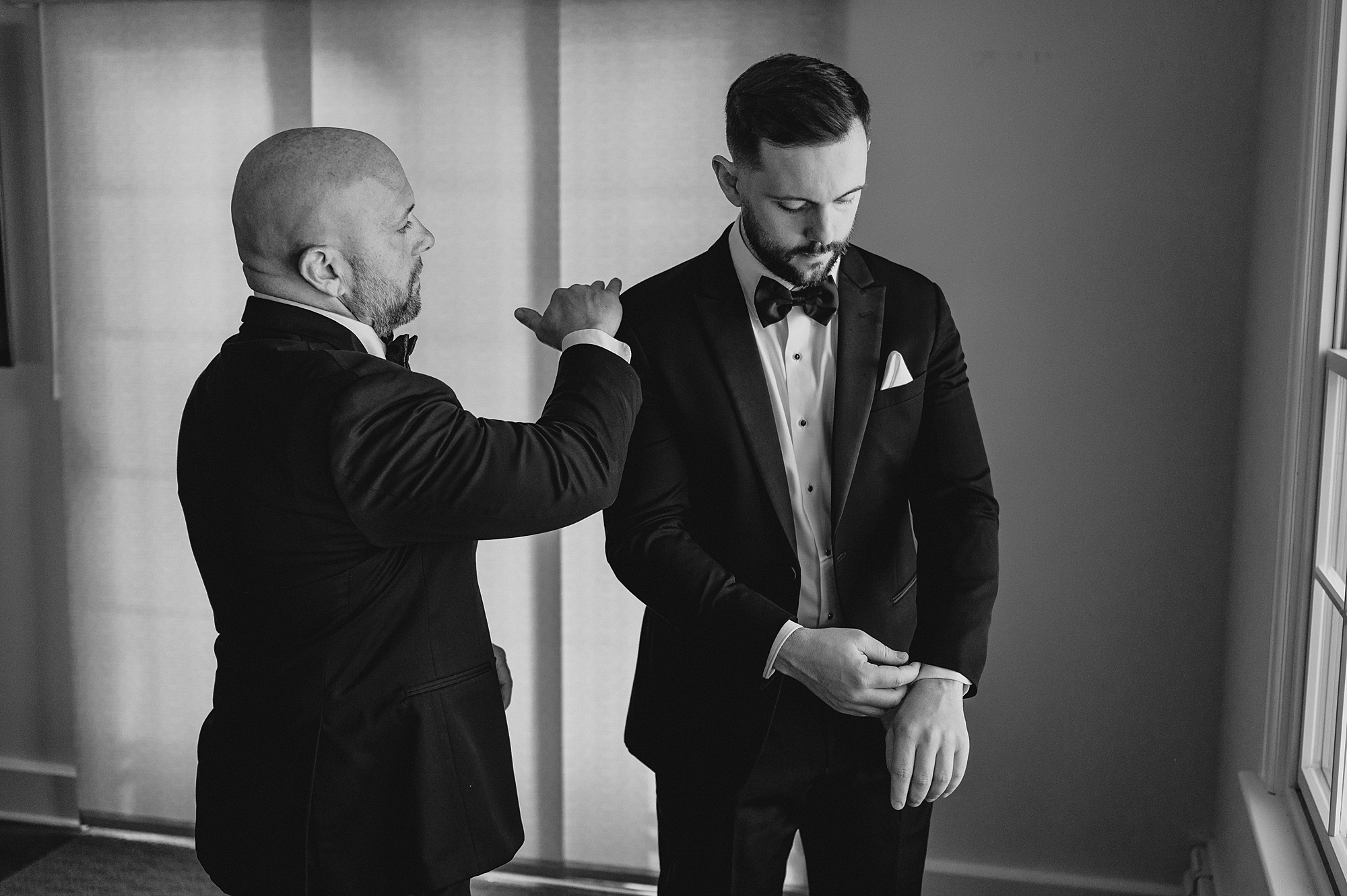 groomsman helps groom into suit jacket and brushes shoulder
