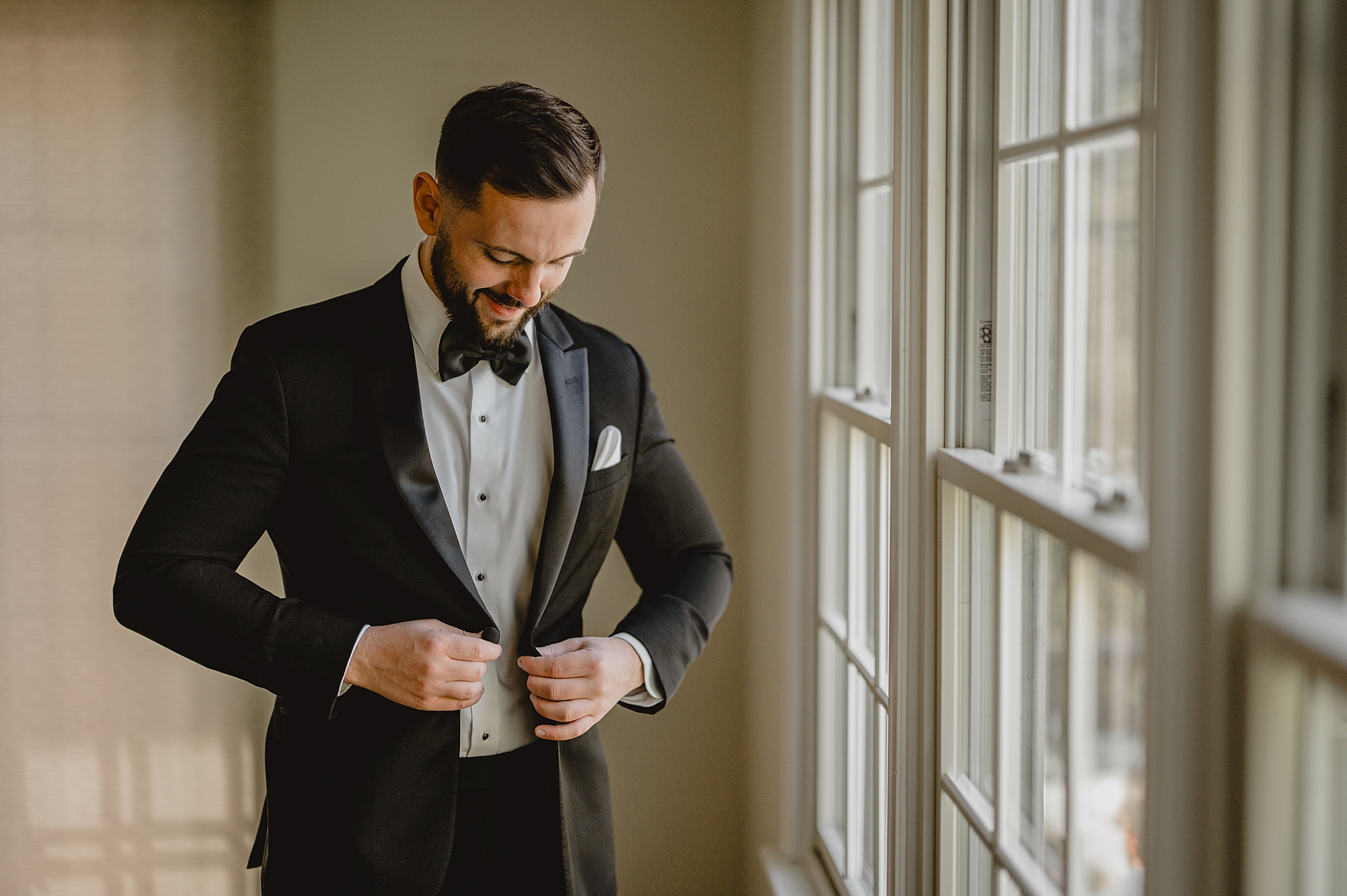 groom buttons up suit jacket by window