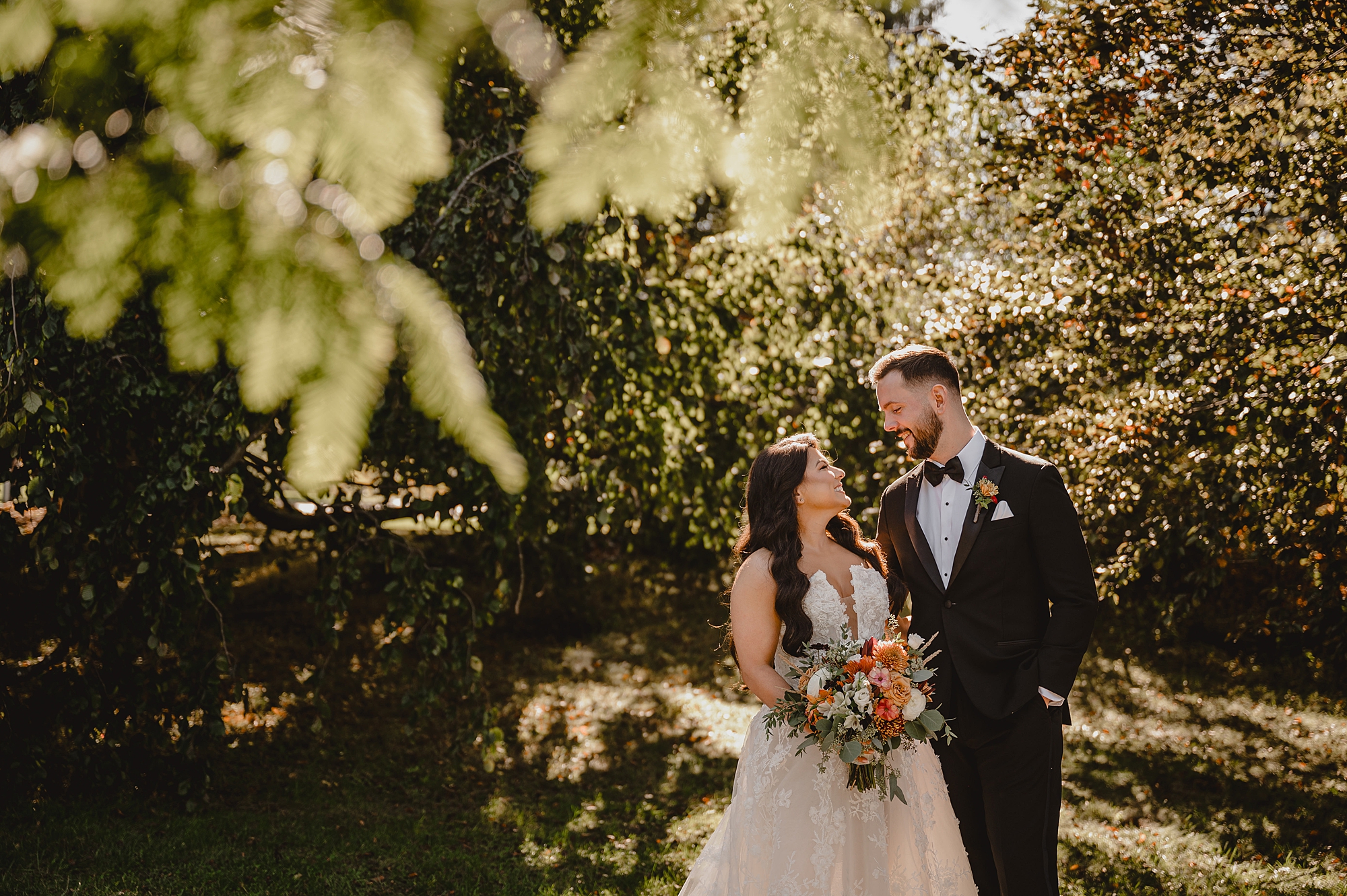 groom smiles at bride standing next to him during fall wedding photos