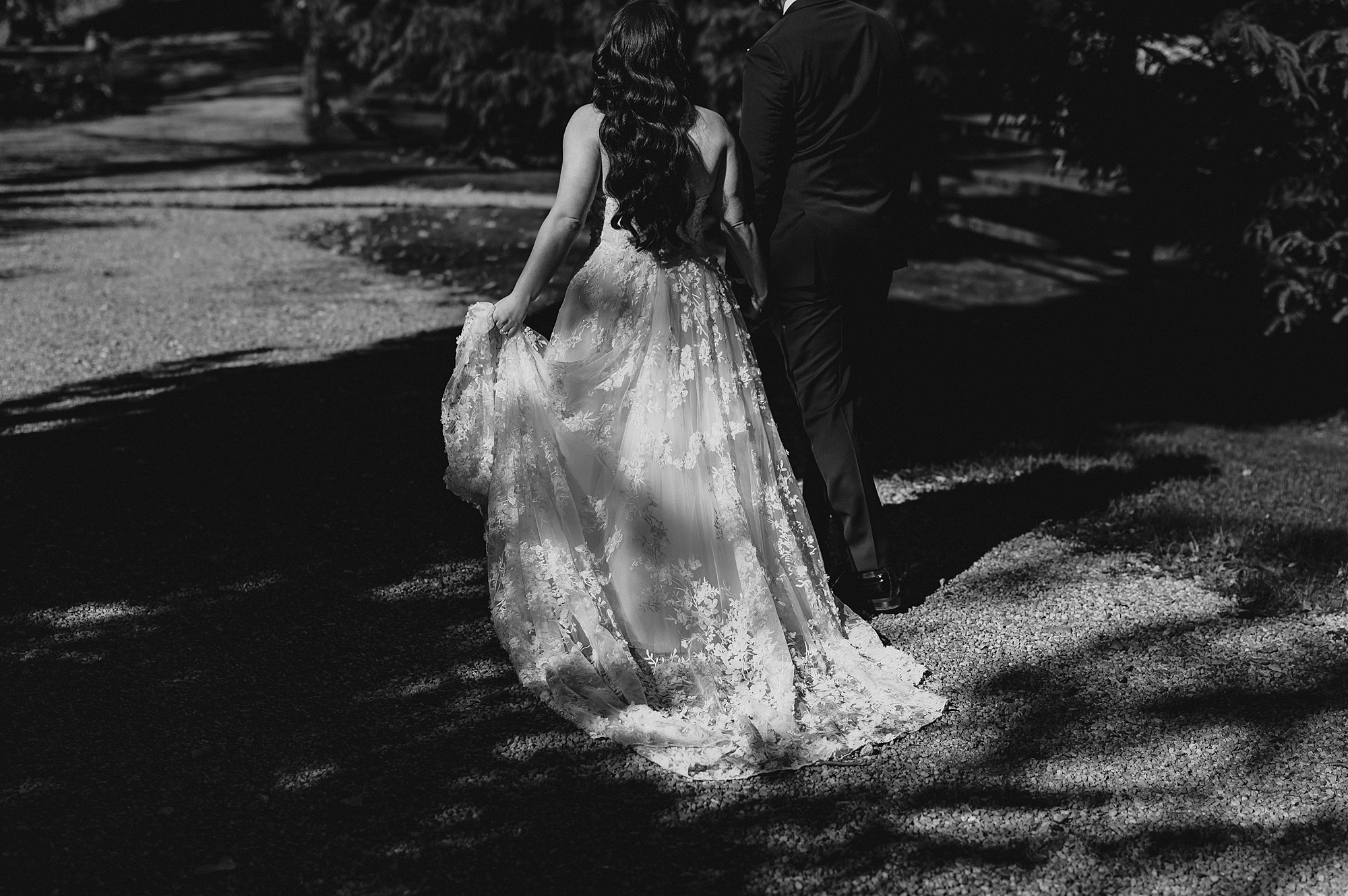 bride holds skirt of wedding gown in one hand, and walks with the groom