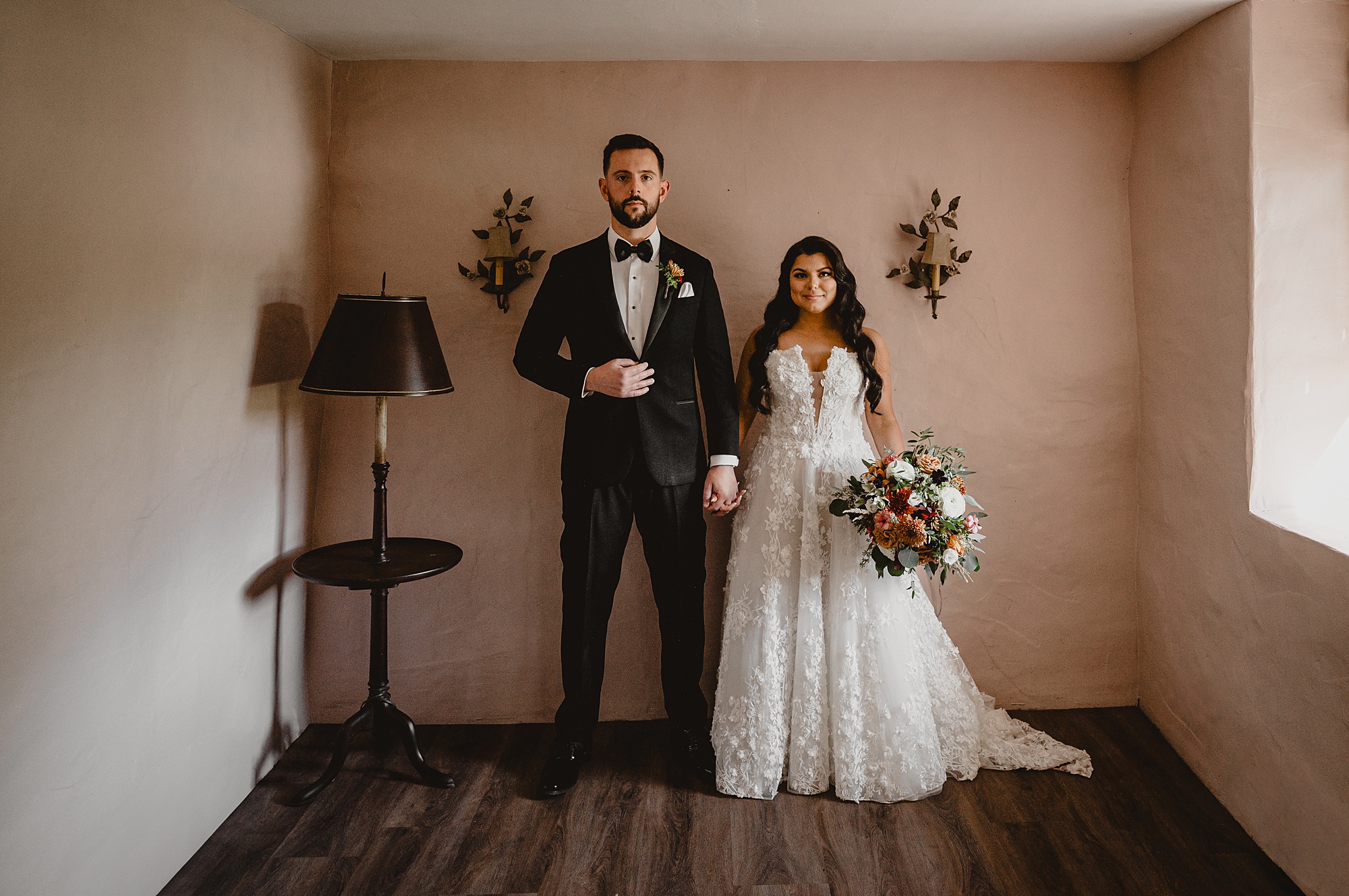 newlyweds hold hands standing inside room with fall flowers at Crossed Keys Estate