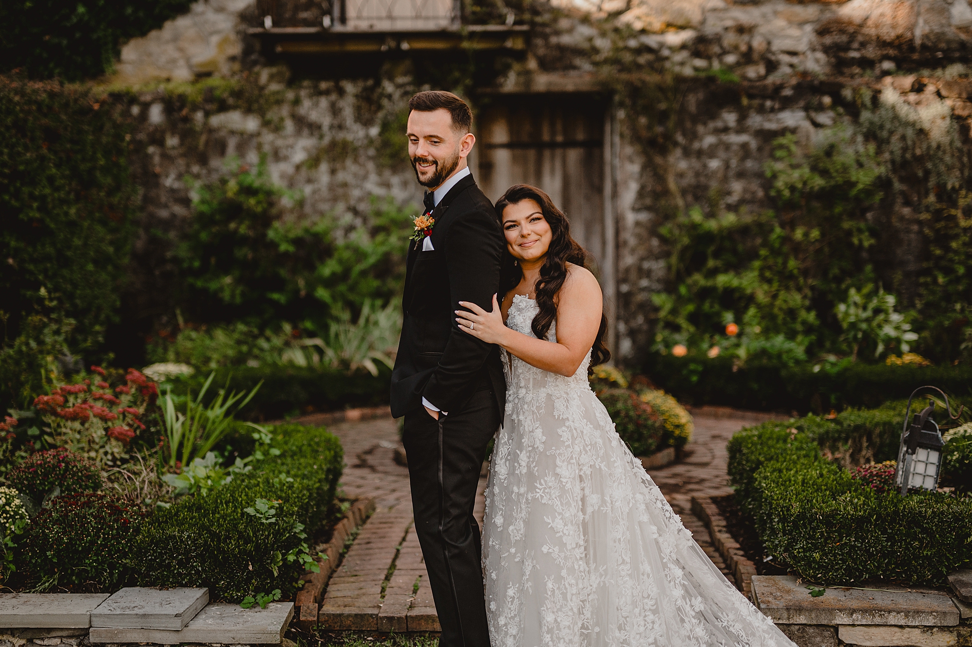 bride stands behind groom leaning on his back in gardens of Crossed Keys Estate