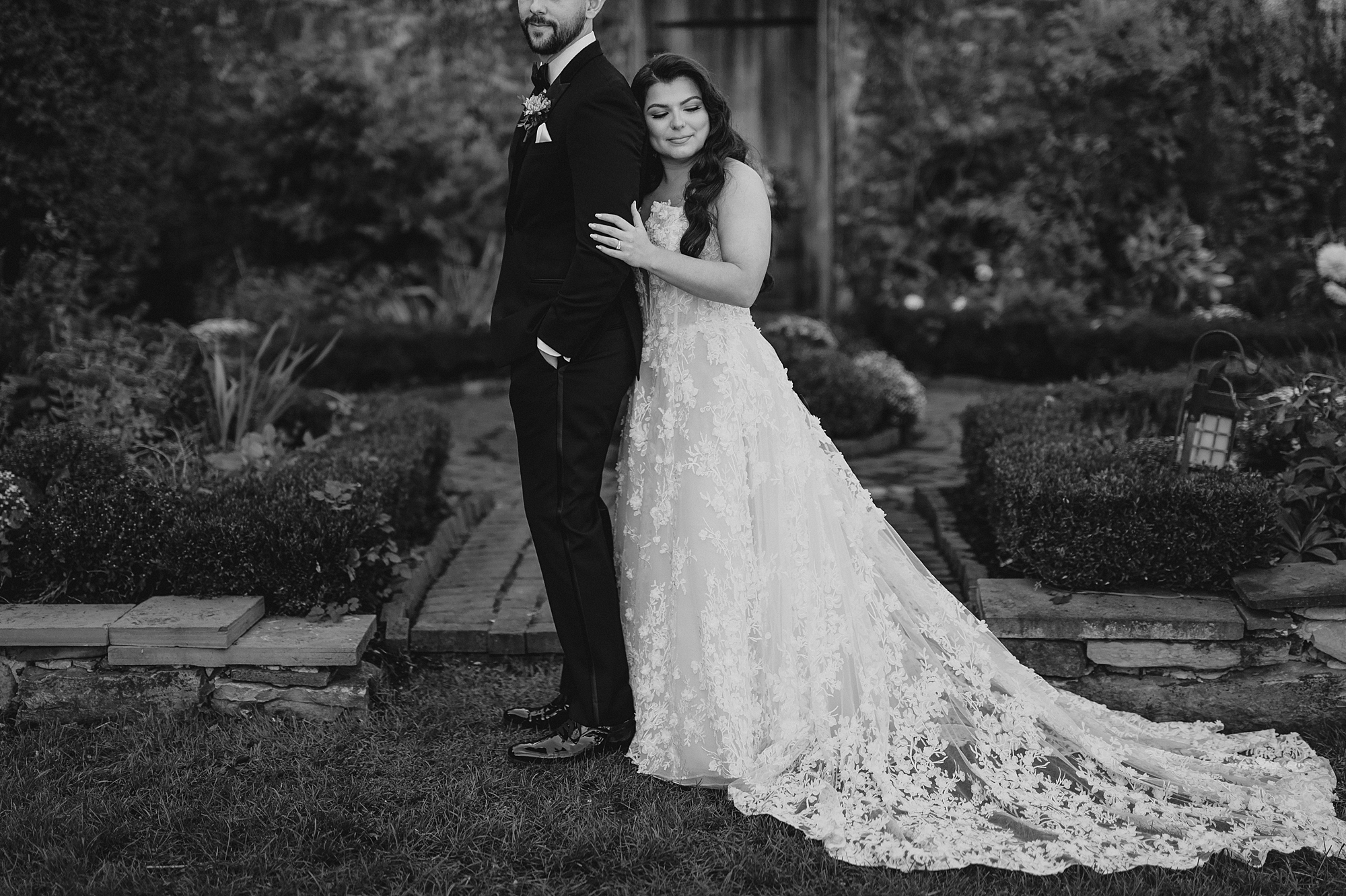 newlyweds stand inside garden of Crossed Keys Estate with bride leaning on groom's back