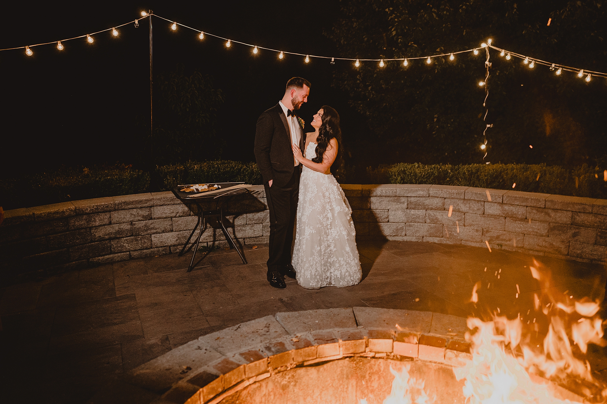 bride and groom pose by fire pit on brick patio at Crossed Keys Estate