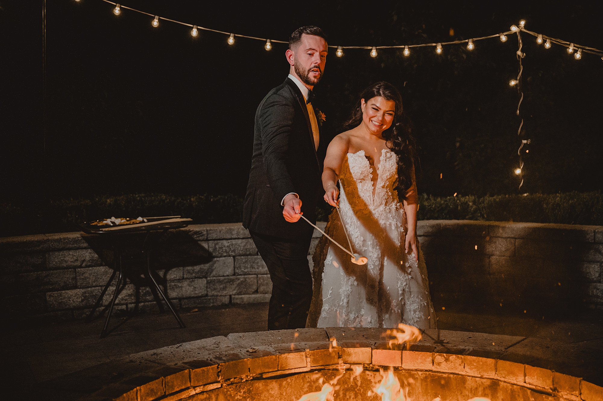 bride and groom pose by fire pit on brick patio at Crossed Keys Estate