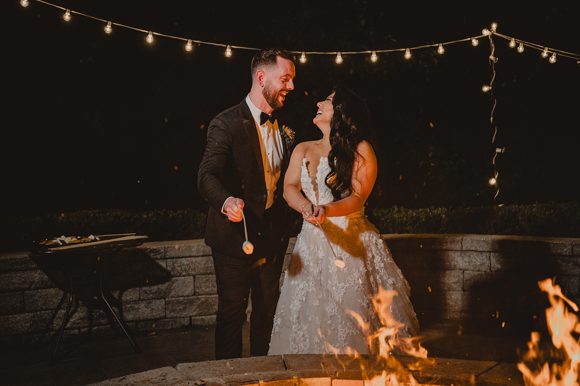 bride and groom pose by fire pit on brick patio at Crossed Keys Estate