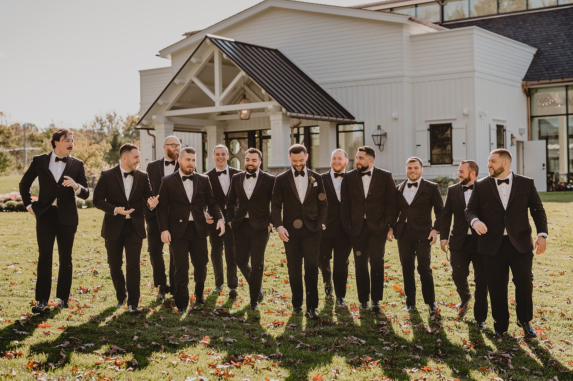 groom and groomsmen walk down hill outside white farm house