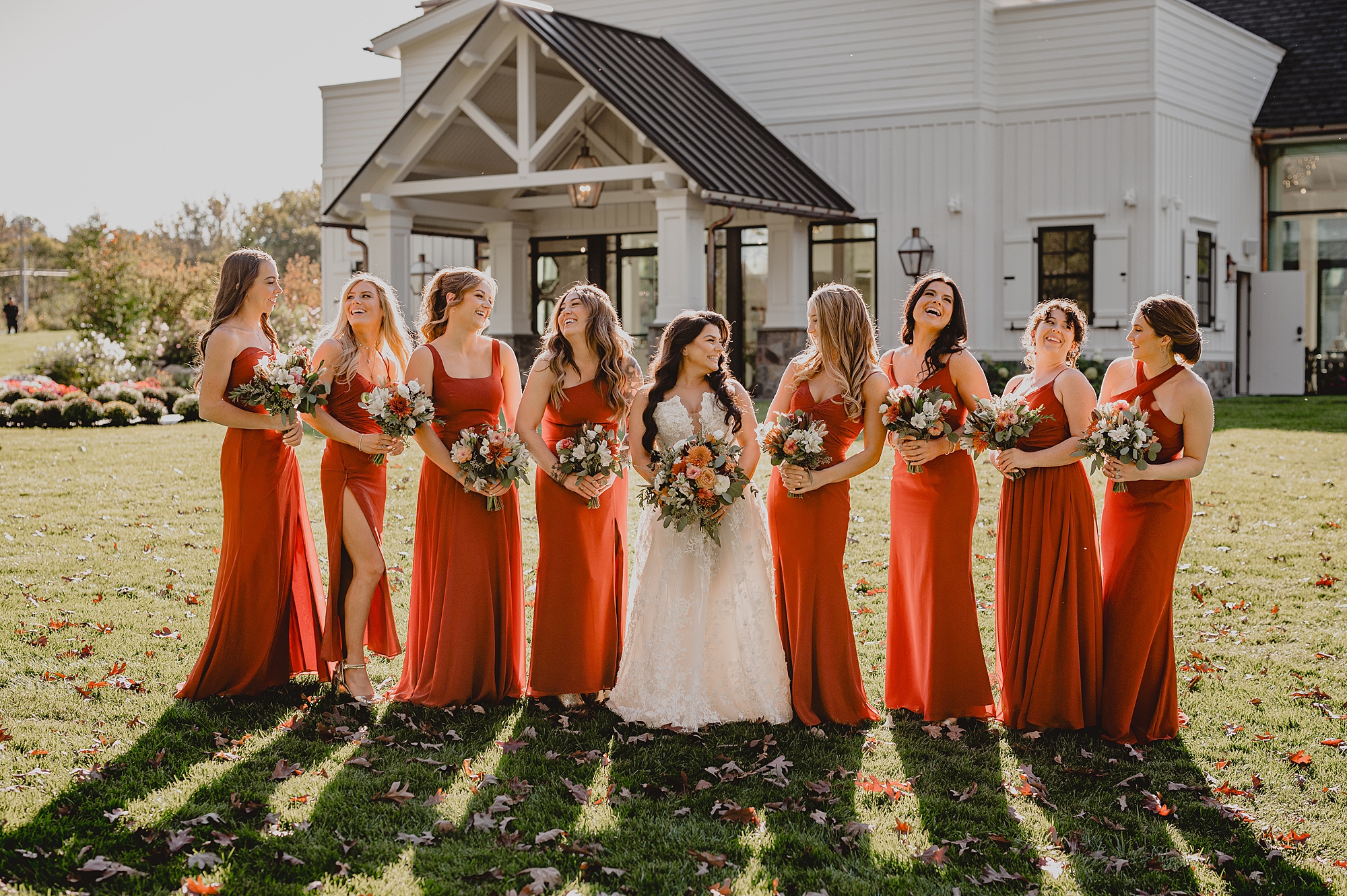 bride stands with bridesmaids in burnt orange gowns outside farm house at Crossed Keys Estate