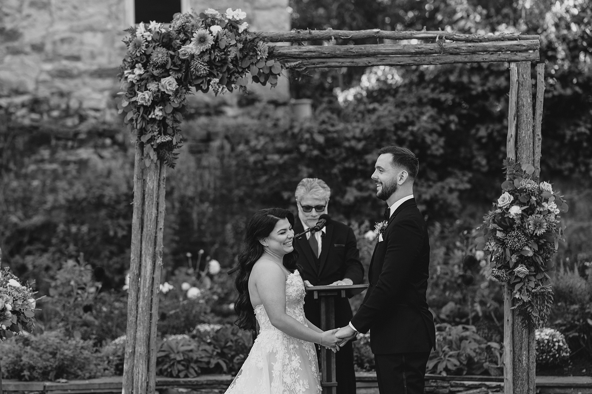 newlyweds hold hands during wedding ceremony on lawn at Crossed Keys Estate