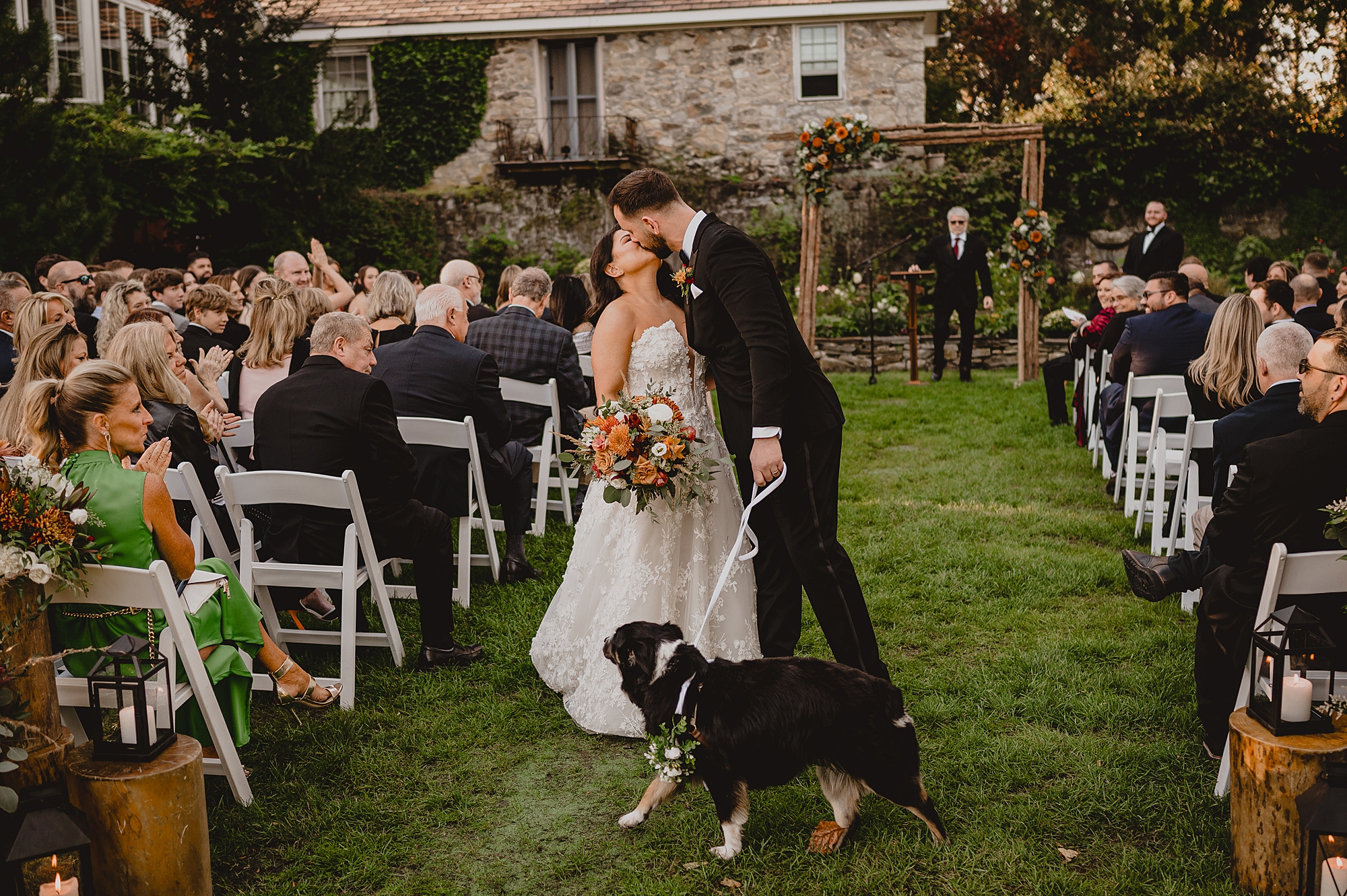 bride and groom kiss while holding dog on leash after ceremony