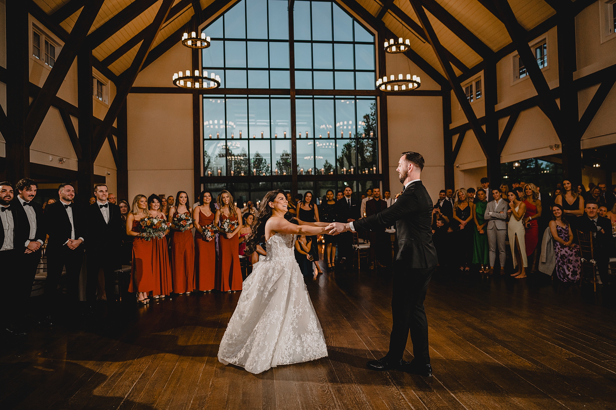 newlyweds hold hands dancing with wedding party behind them