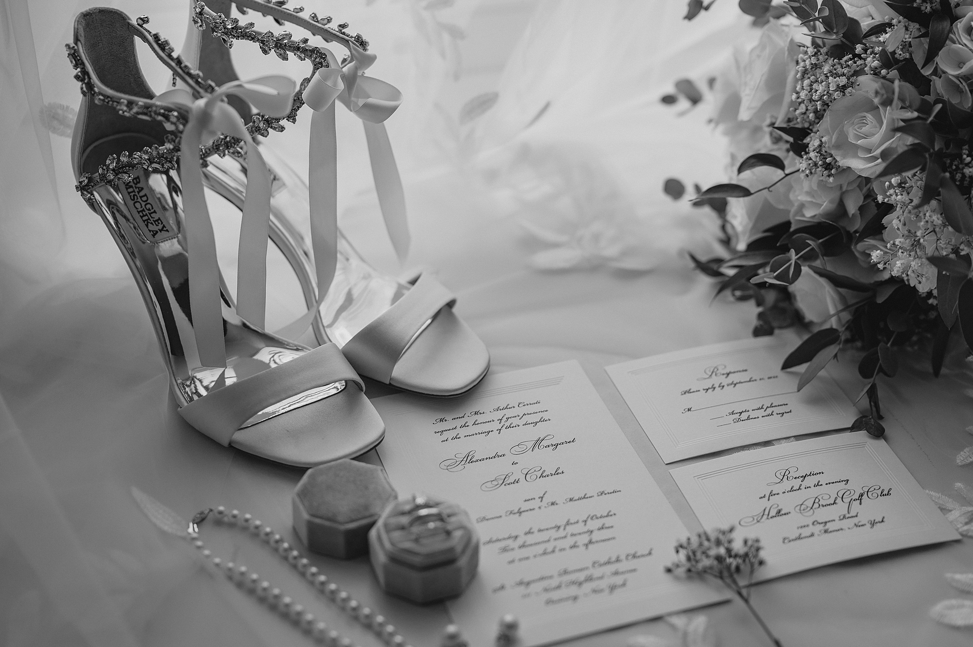 black and white photo of bride's shoes, invitation suite, and rings in boxes
