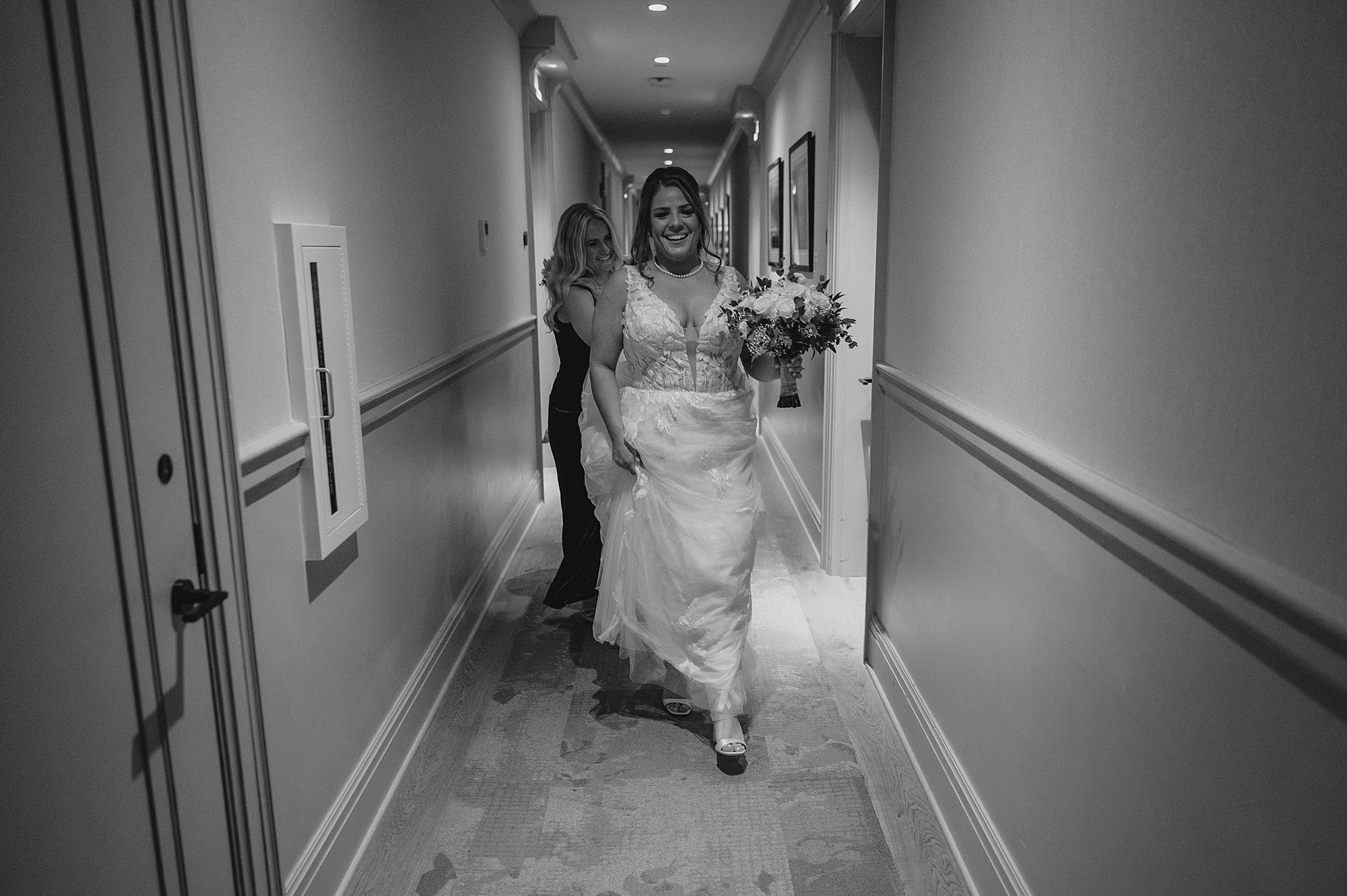 bride walks down hallway of hotel with mom carrying her skirt
