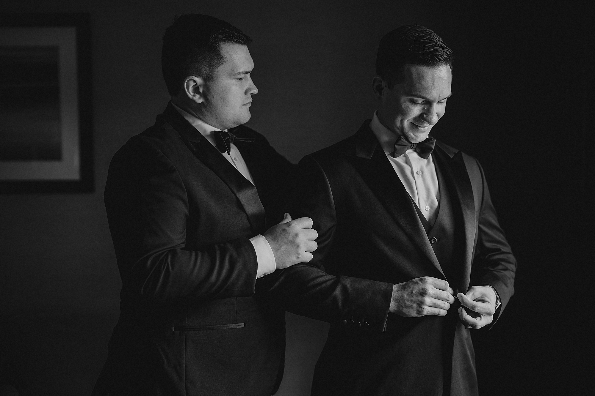 groomsman helps groom with suit jacket 