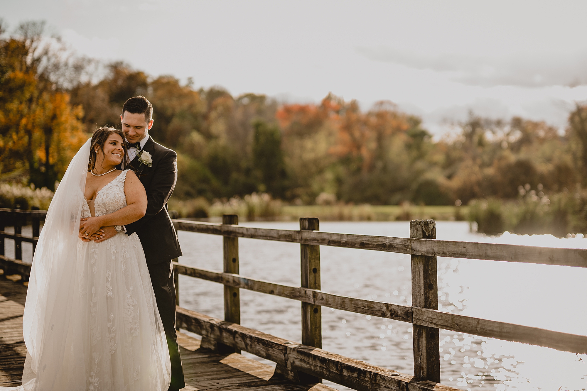 groom hugs bride from behind by fence line at Hollow Brook Golf Club