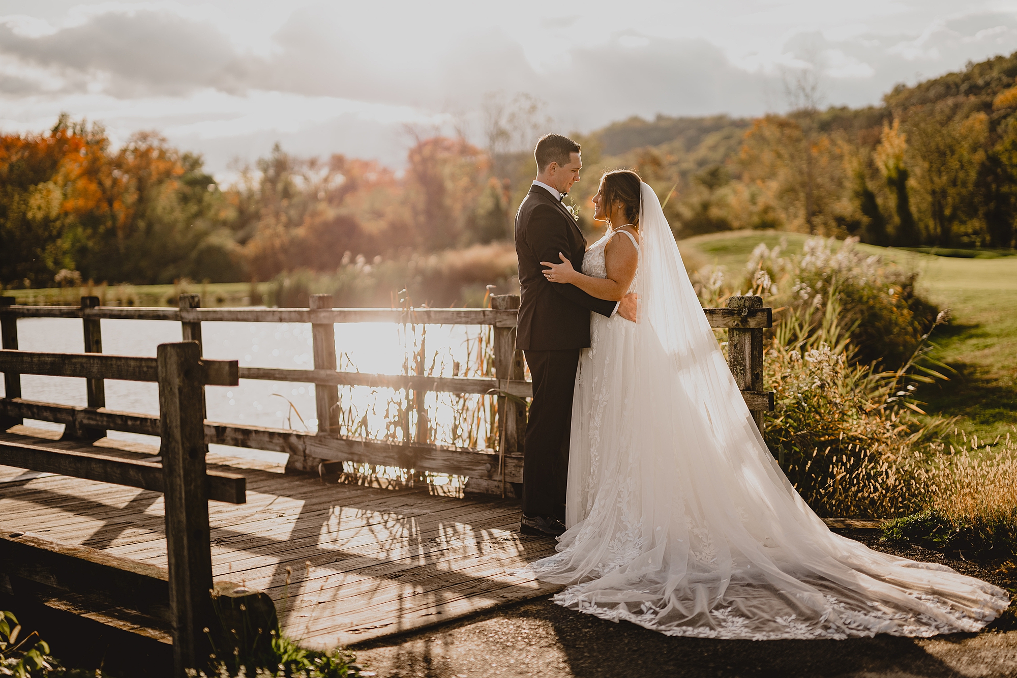 bride and groom hug by wooden fence at sunset at Hollow Brook Golf Club