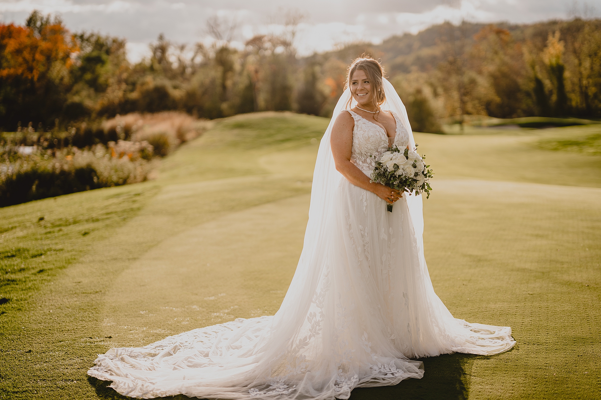 bride stands holding bouquet of white flowers on golf course at Hollow Brook Golf Club