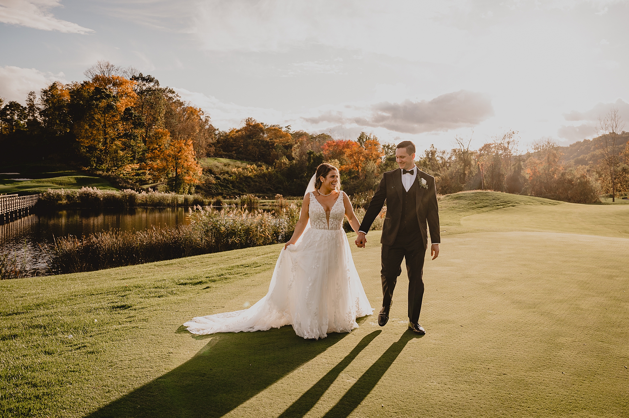 newlyweds hold hands walking across putting green at Hollow Brook Golf Club