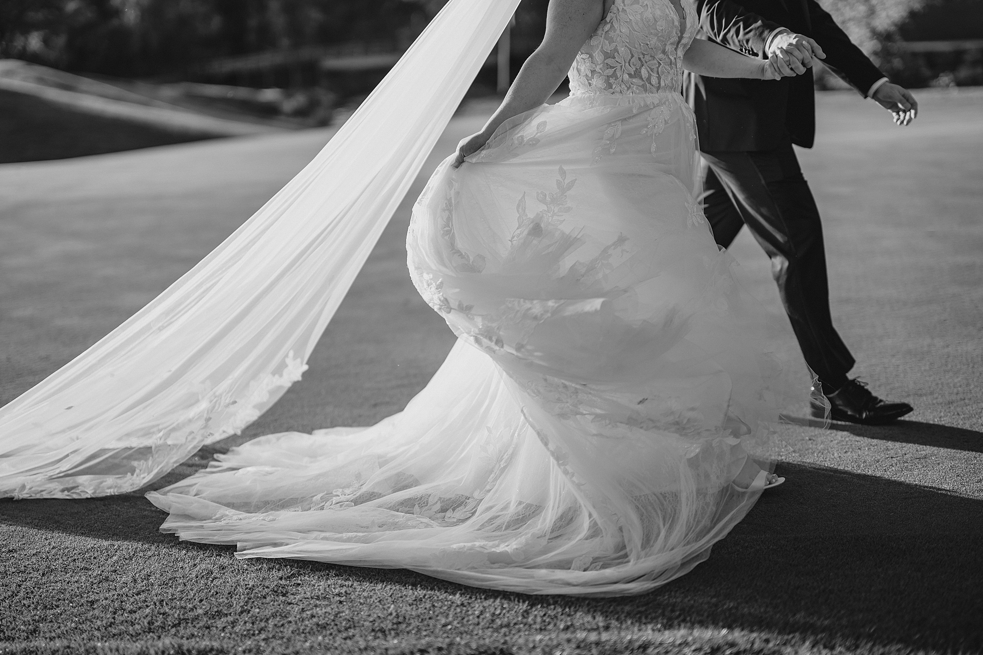 bride moves skirt of wedding dress walking on golf course 
