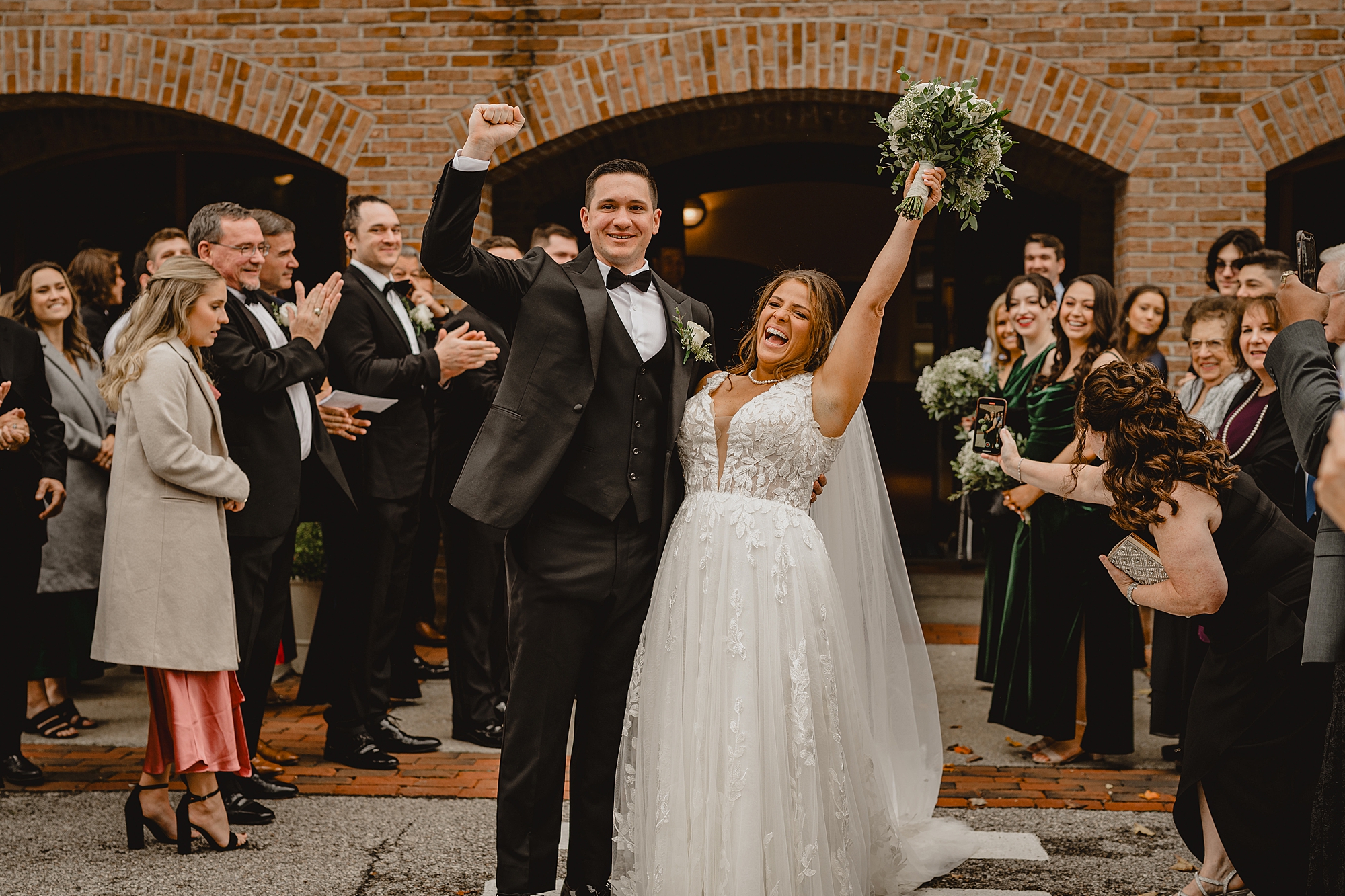 bride and groom cheer leaving stone church with guests around them