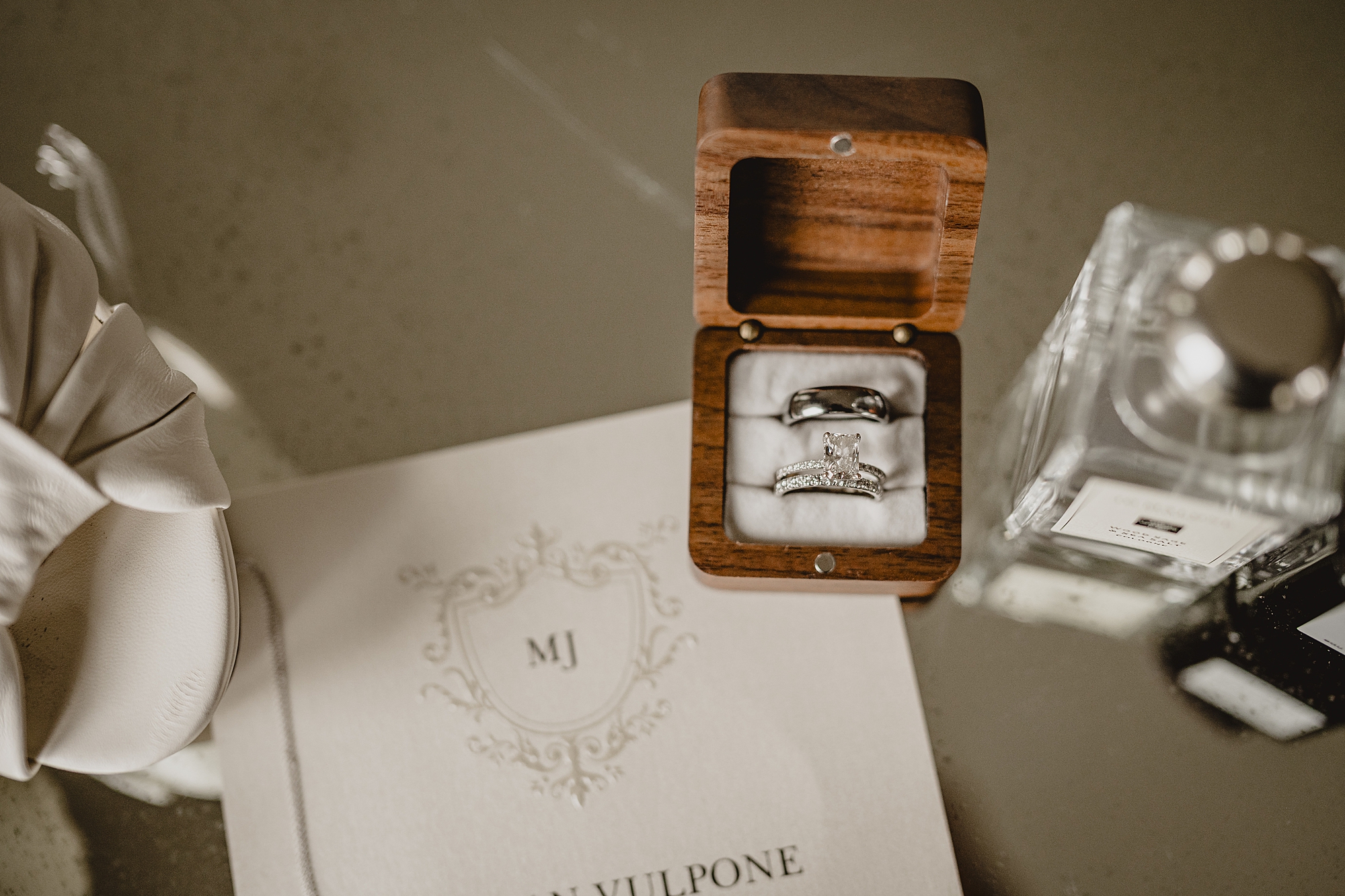 wedding rings in wooden box sitting on custom monogramed invitations 