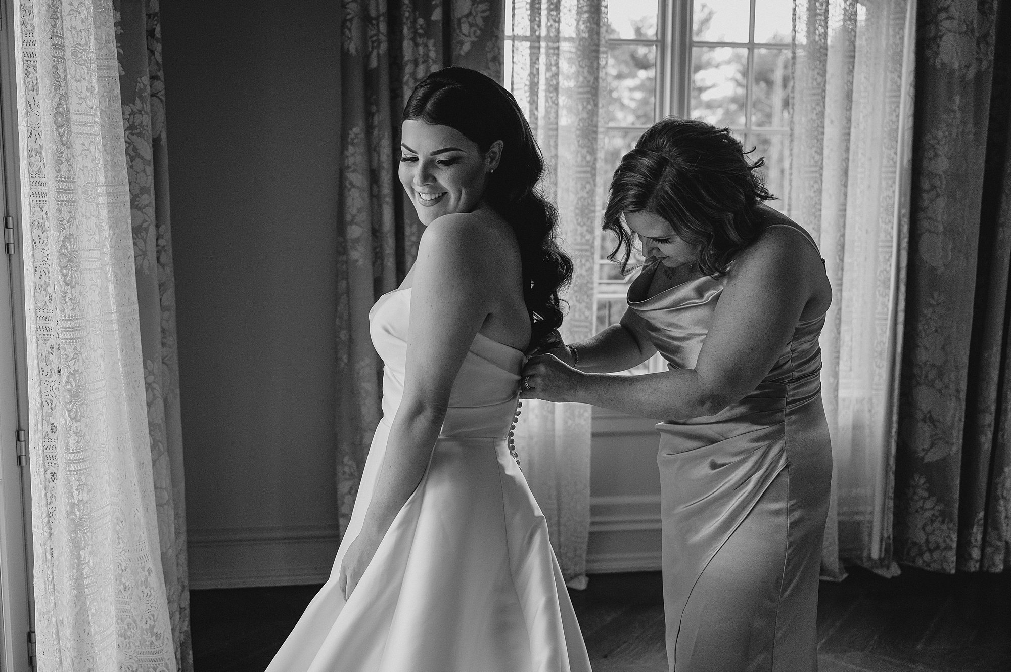 bridesmaid helps bride into wedding gown in bridal suite at Park Chateau
