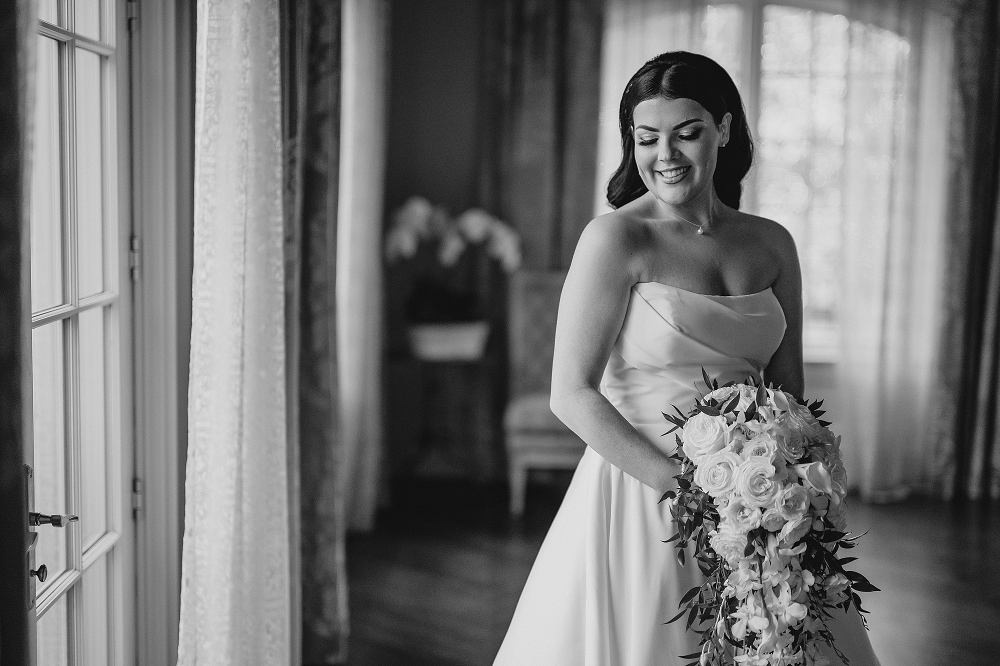 bride holds cascading bouquet in front of strapless gown in bridal suite at Park Chateau