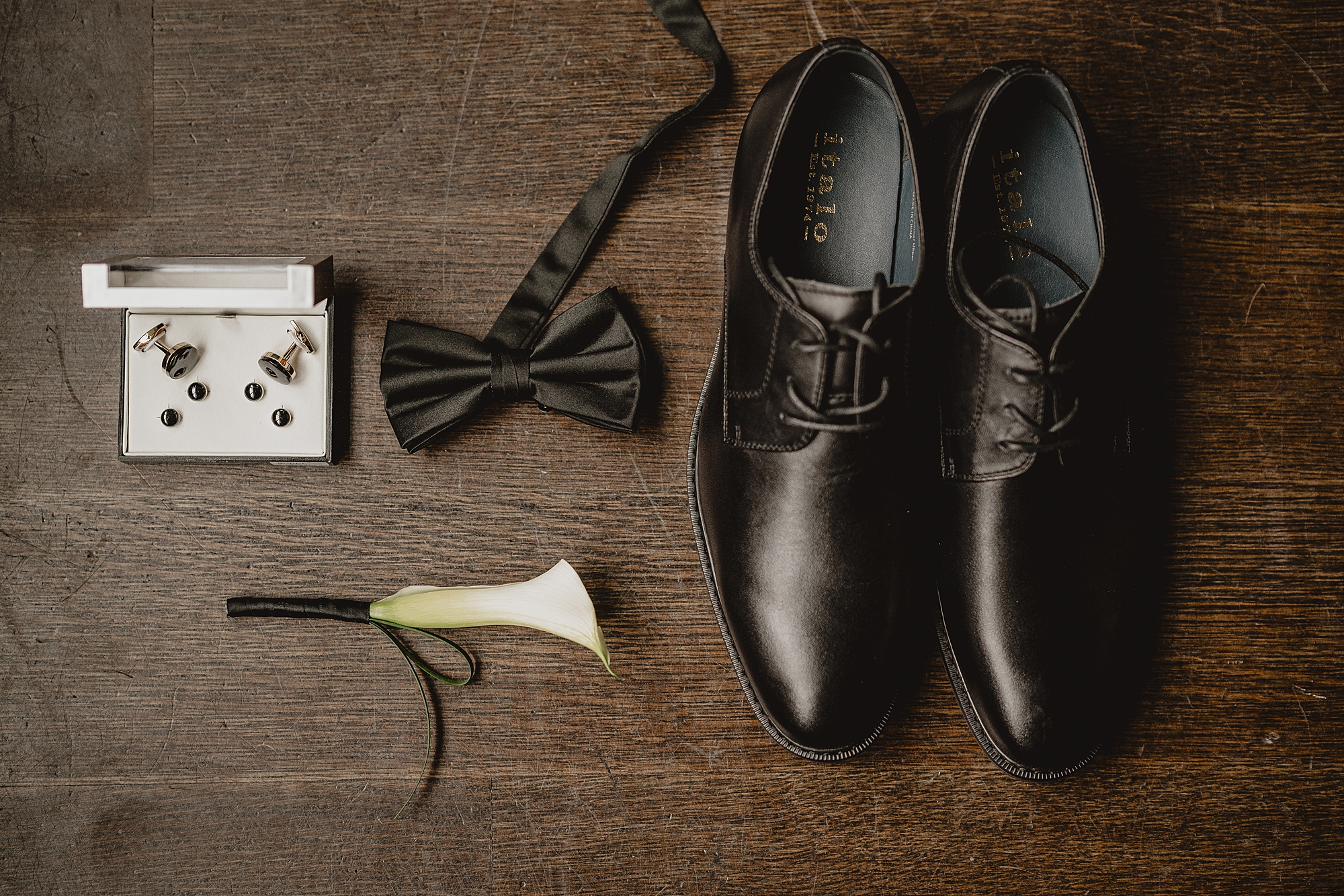 groom's black shoes, bow tie, and calla lily for wedding day