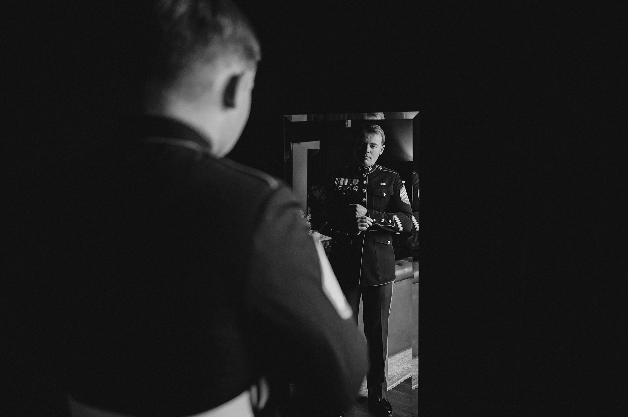 Marine adjusts belt on uniform looking in mirror reflection 